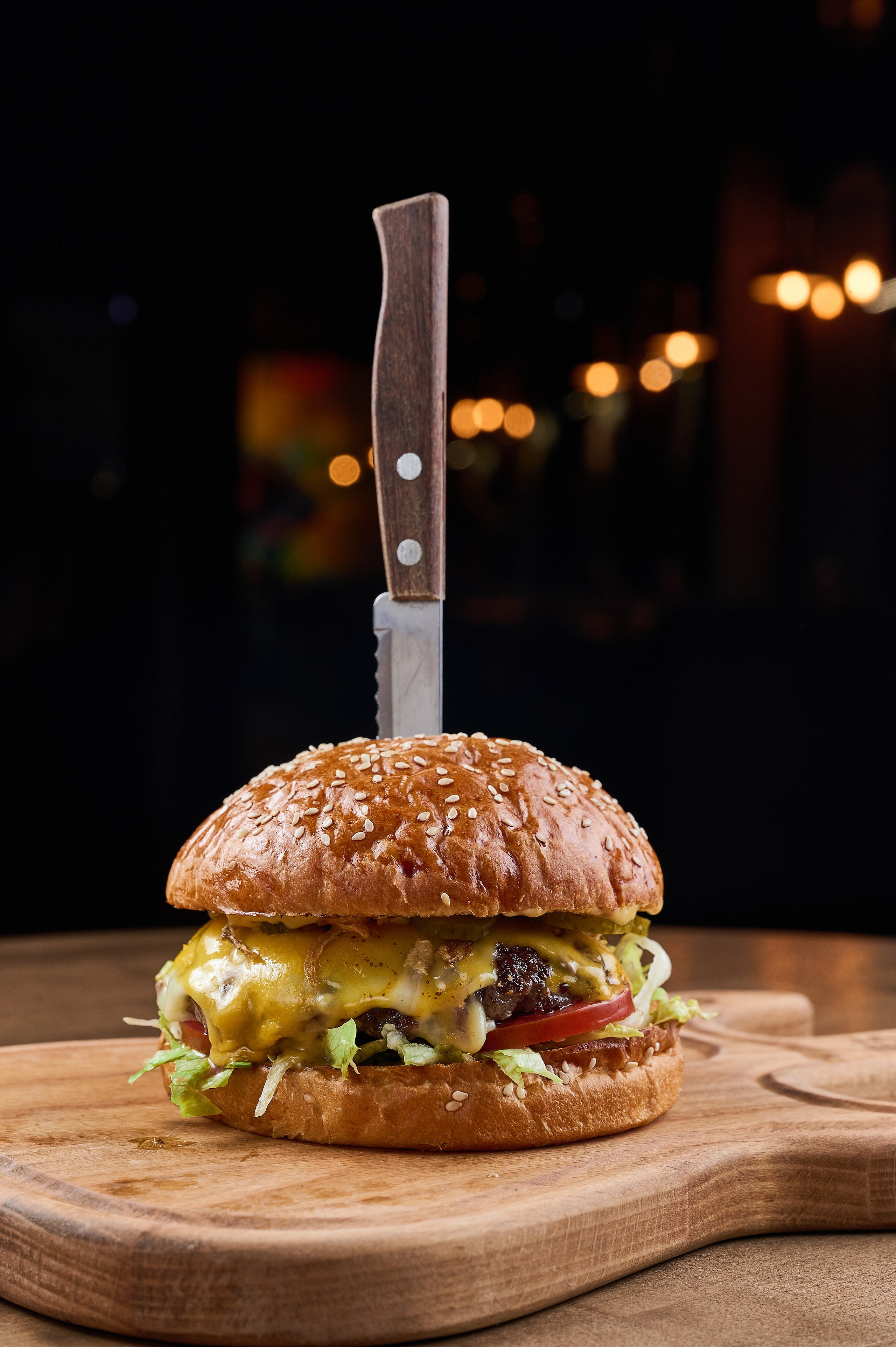 Аппетитный бургер в разрезе, с стекающим соусом и свежими овощами на деревянной доске. Яркая фуд-фотография, сделанная в Екатеринбурге