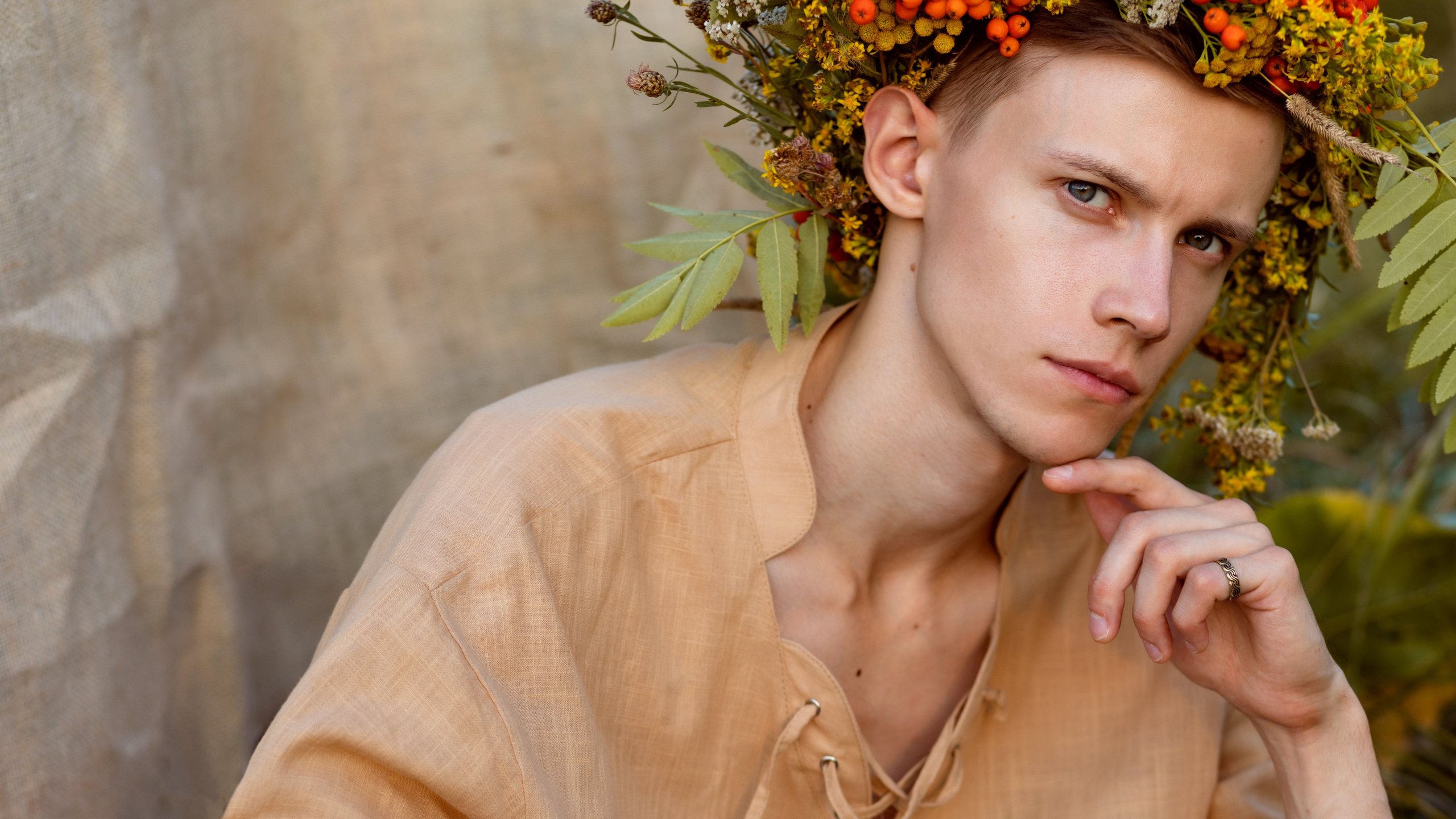 Молодой парень в коричневой рубахе с венком из трав на голове