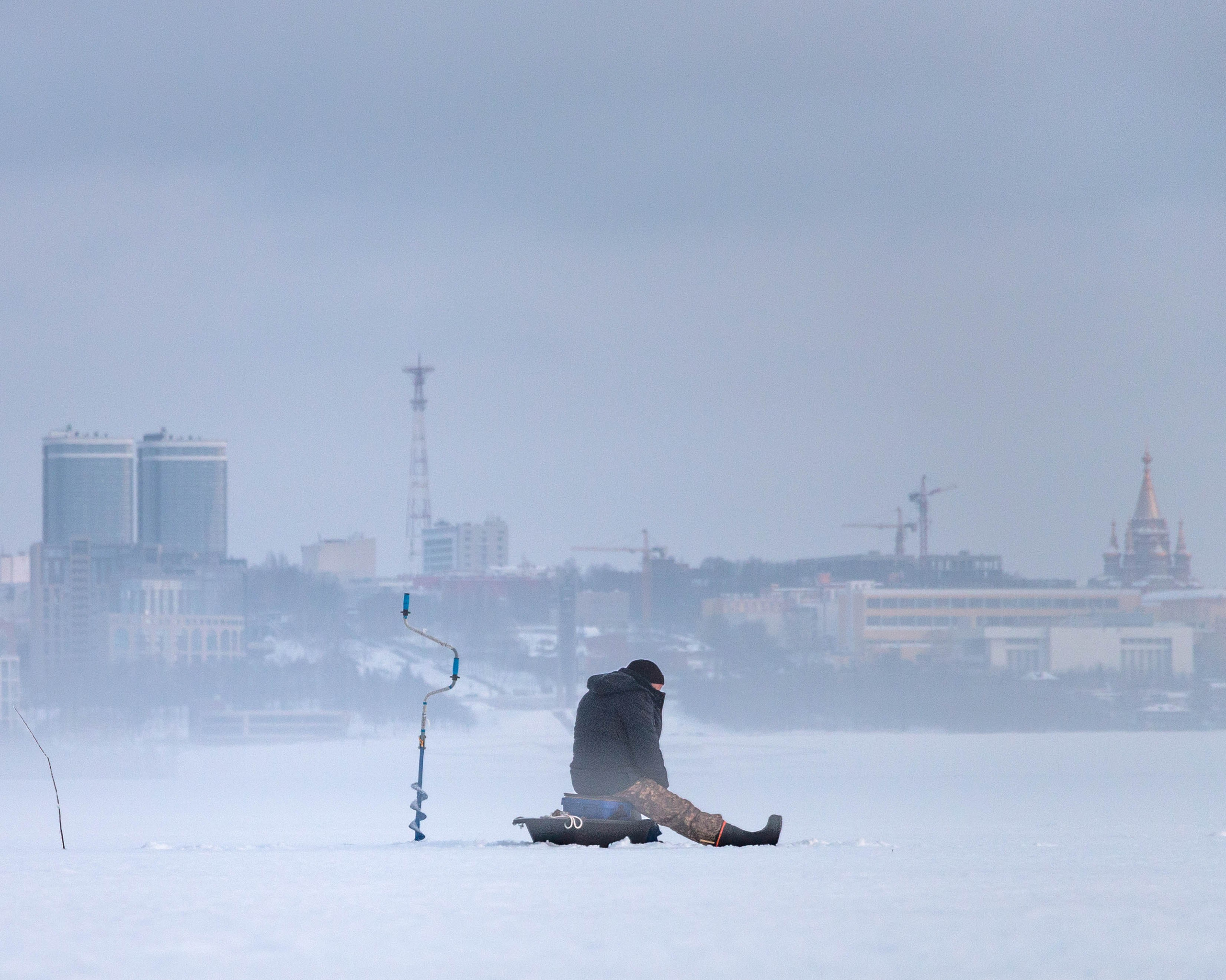 Одинокий рыбак сидит на пруду уткнувшись в лунку