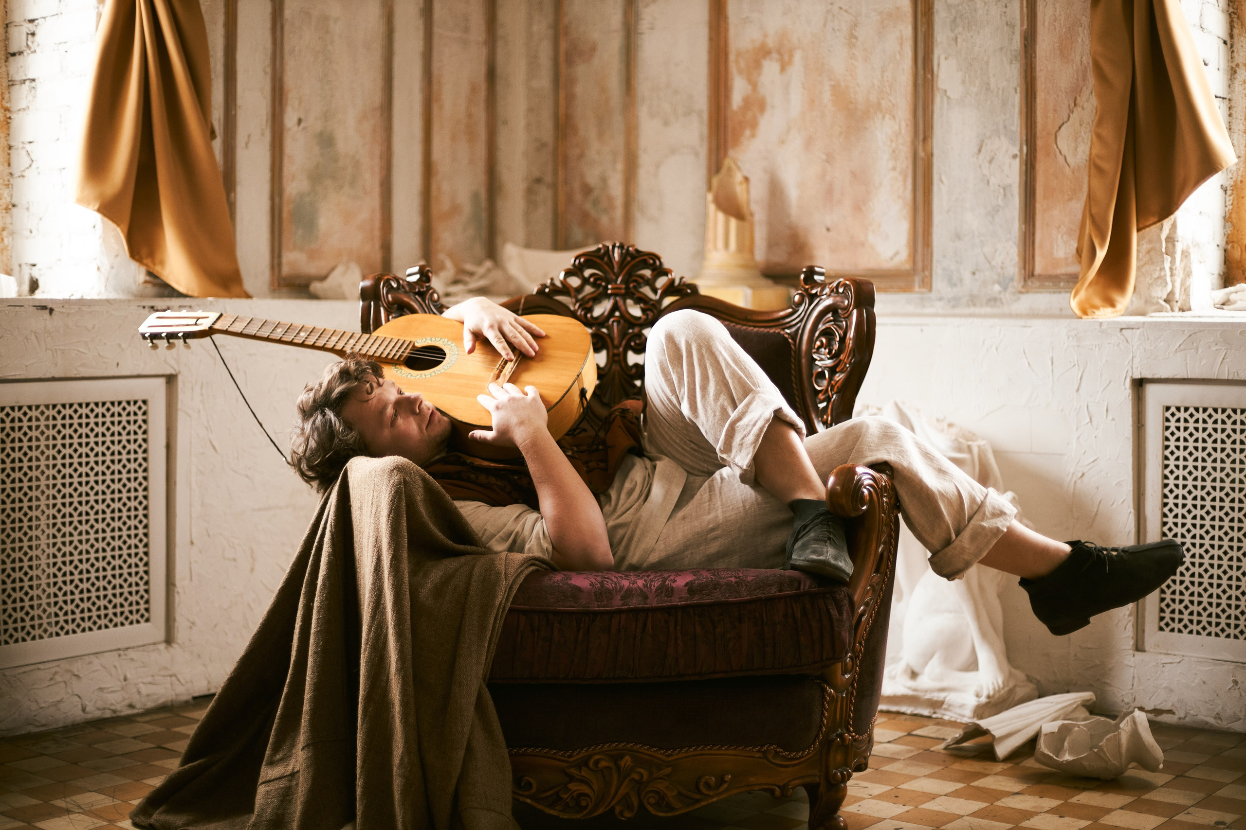 Актёр Сергей Друзьяк играет на гитаре, лёжа в кресле. Стилизованная фотосессия