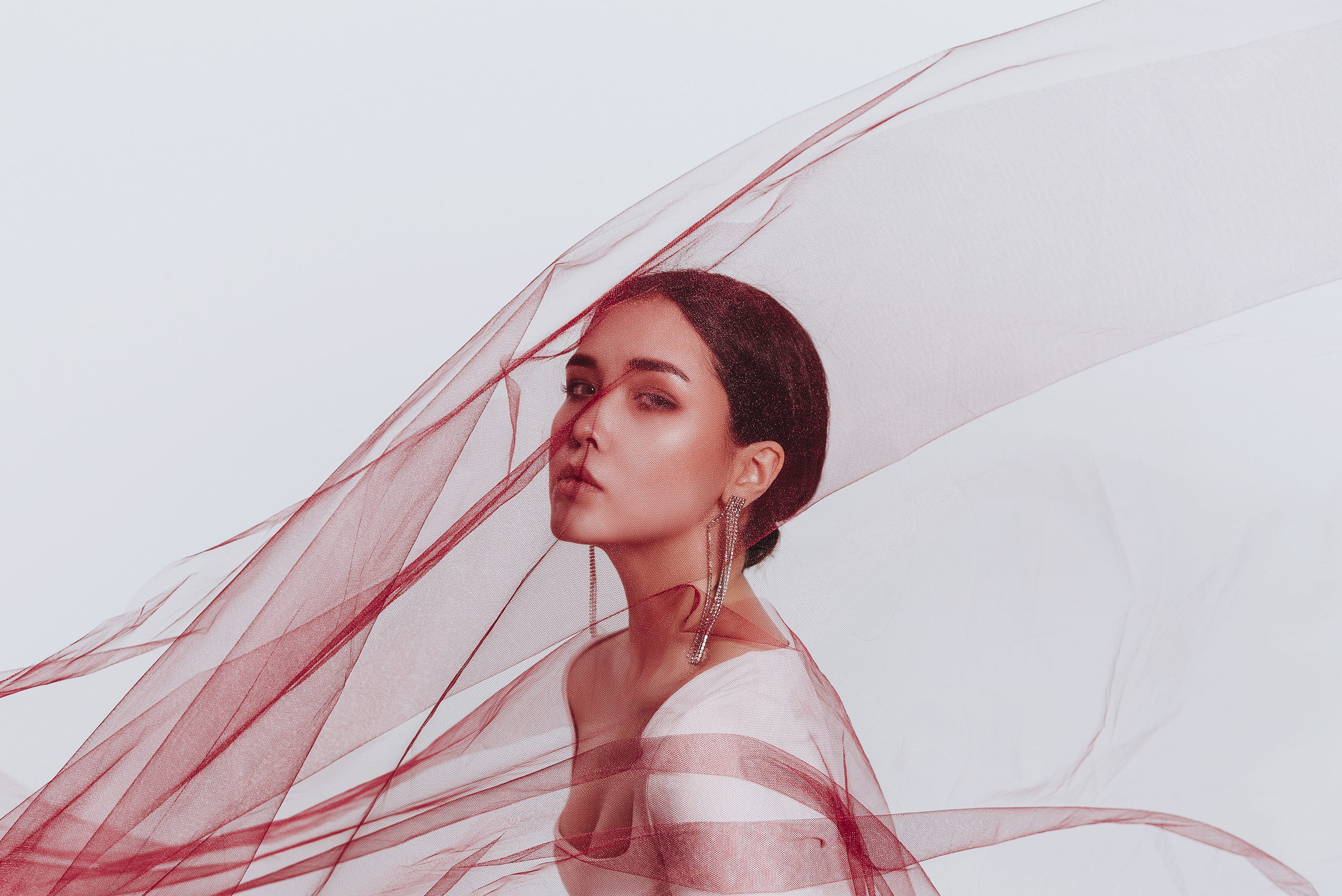 Красивая легкая красная ткань развивается на лице у девушки.