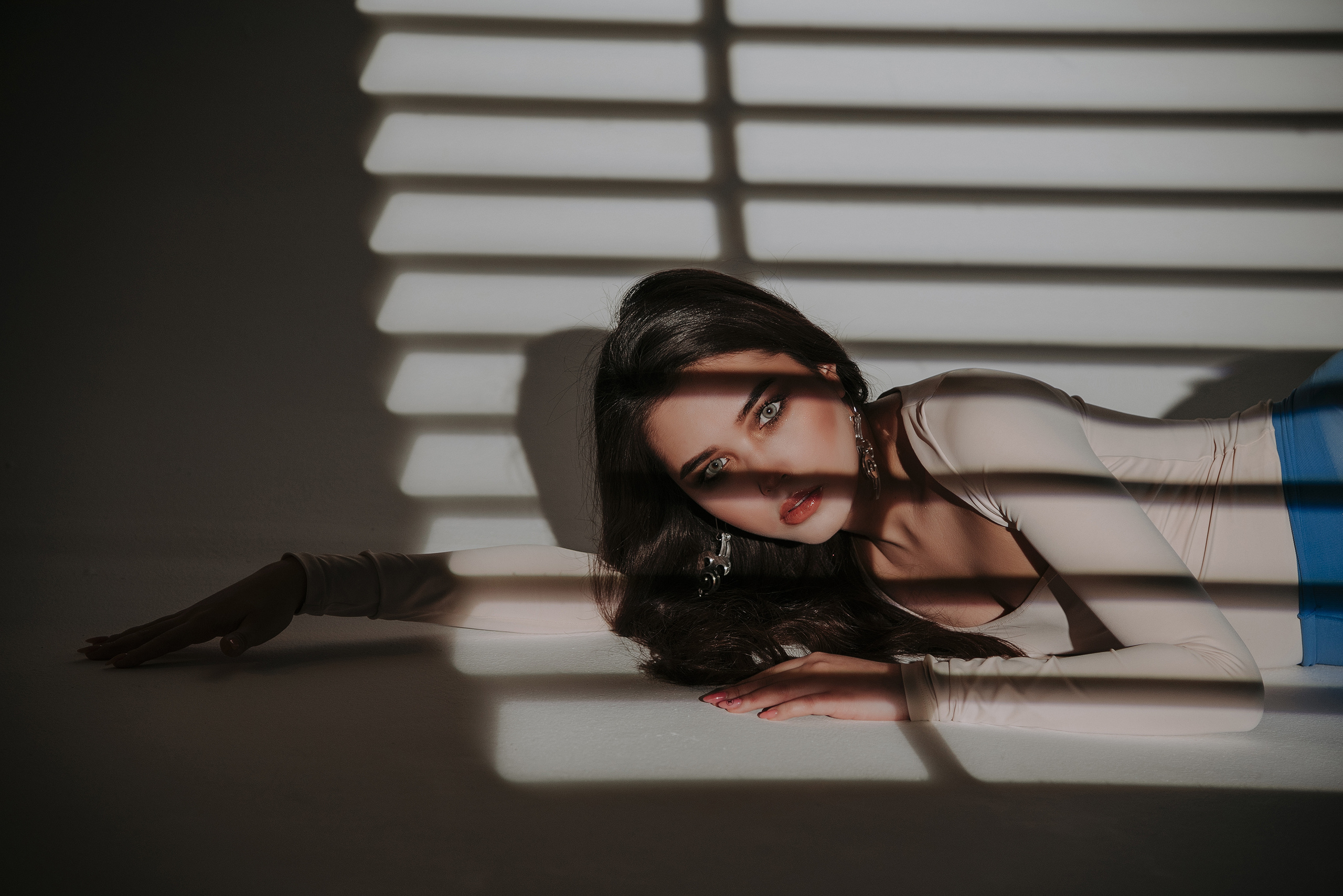Красотка лежит на фоне жалюзи.