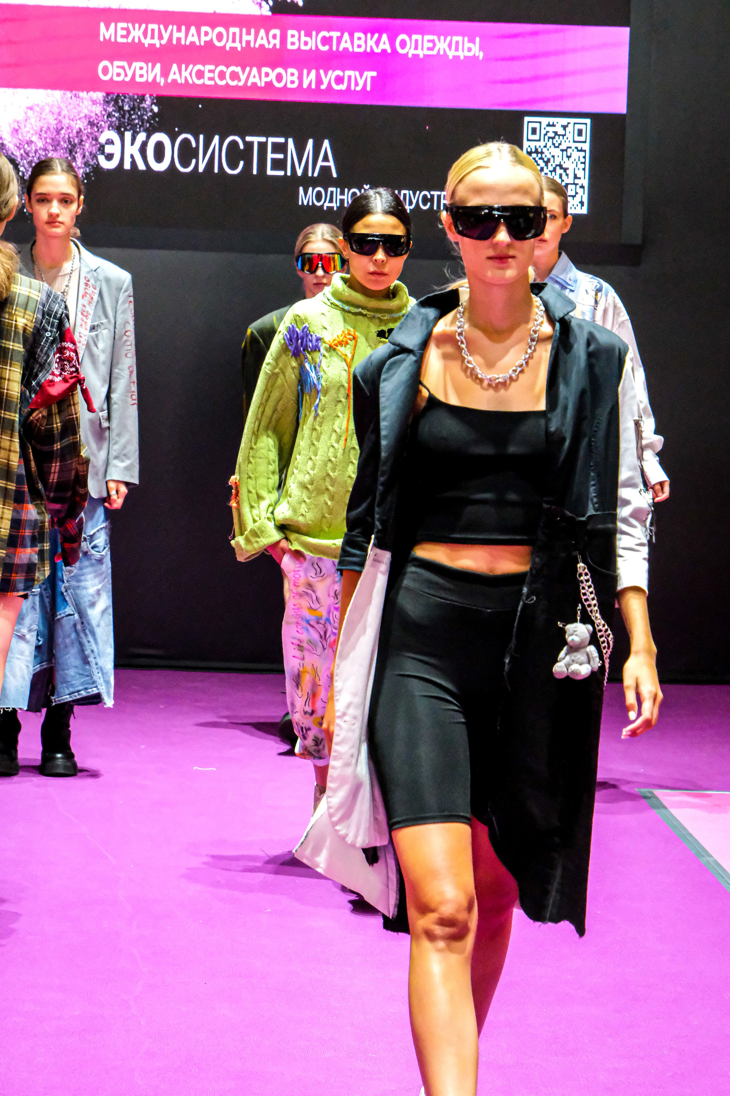  "Модели в ярких нарядах проходят по подиуму во время показа мод, освещенные яркими софитами и окруженные восторженными зрителями."