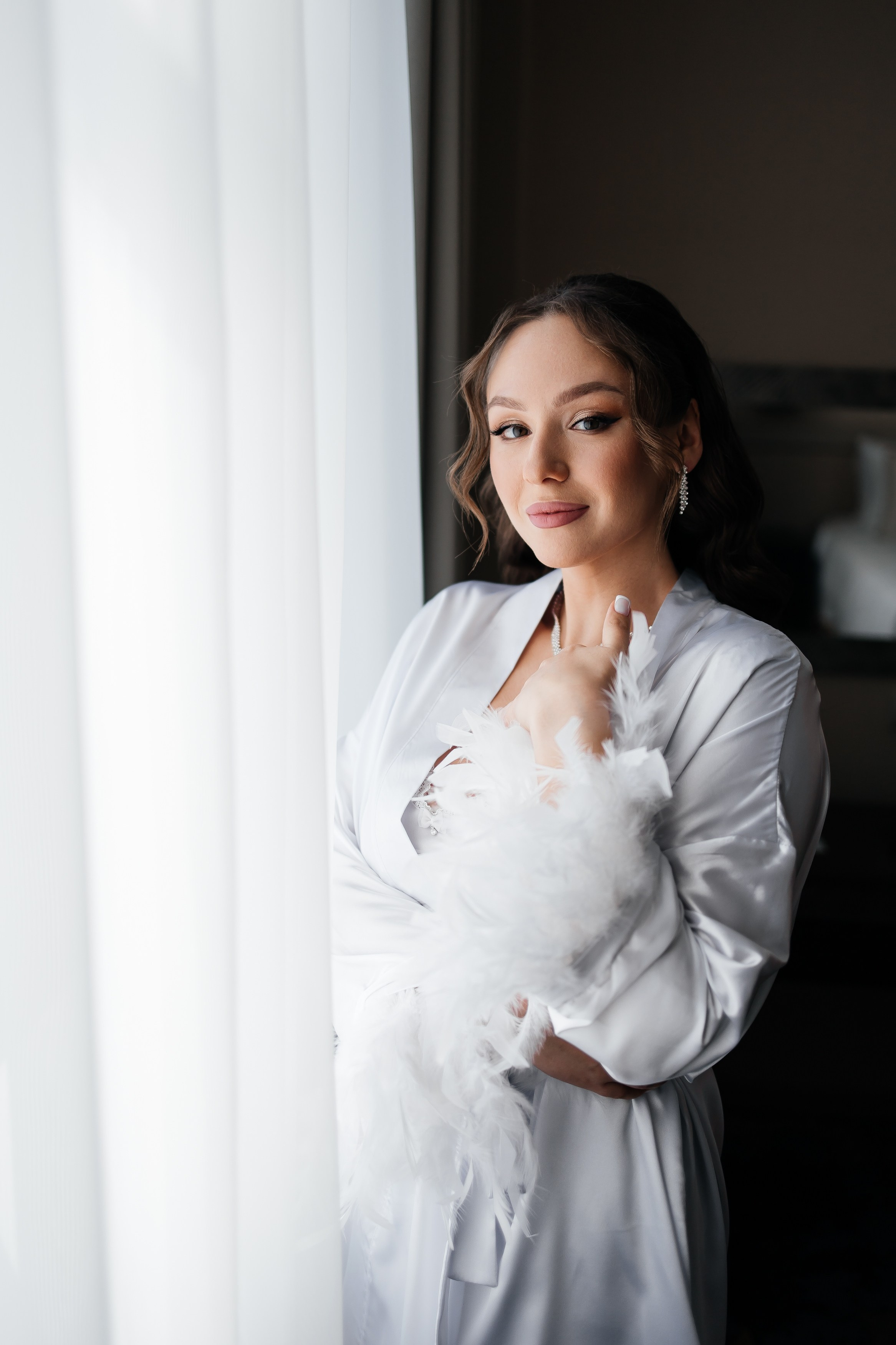 Невеста стоит в сорочке у окна в отеле