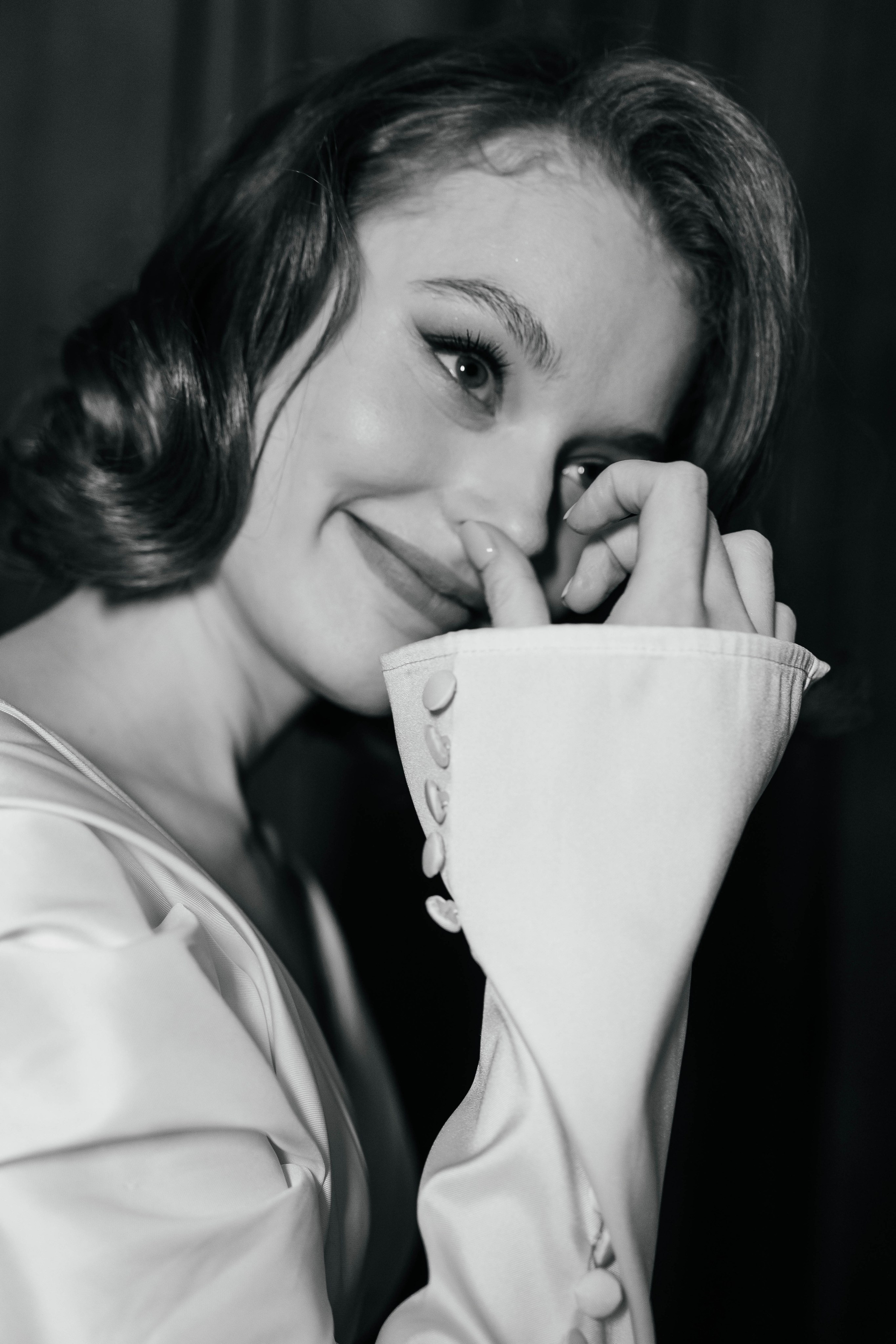 Невеста на чёрно-белом фото улыбается, прикрывая лицо рукой