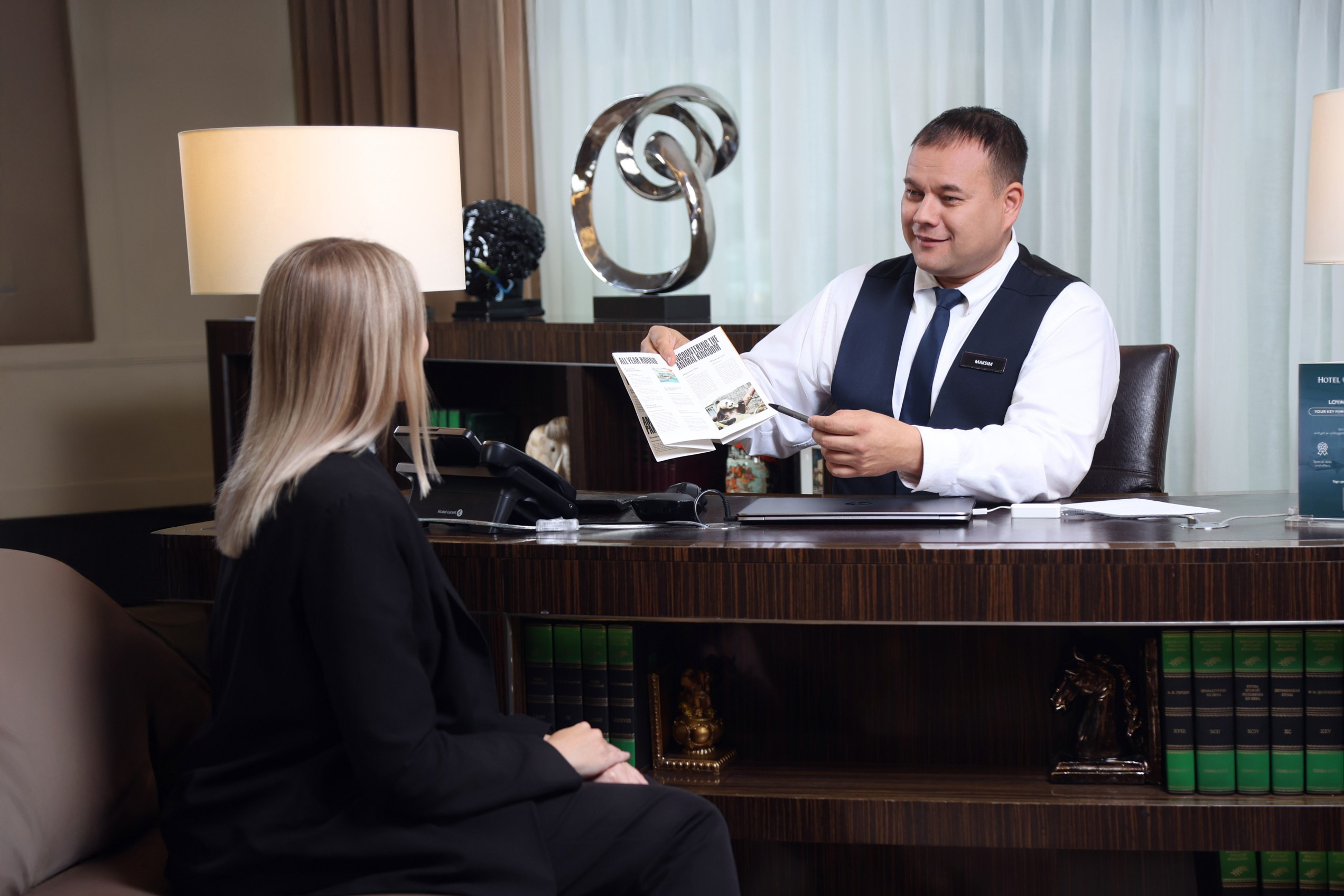 Консьерж в элегантном костюме объясняет гостям маршрут по достопримечательностям Москвы. Профессиональная съемка в лобби.