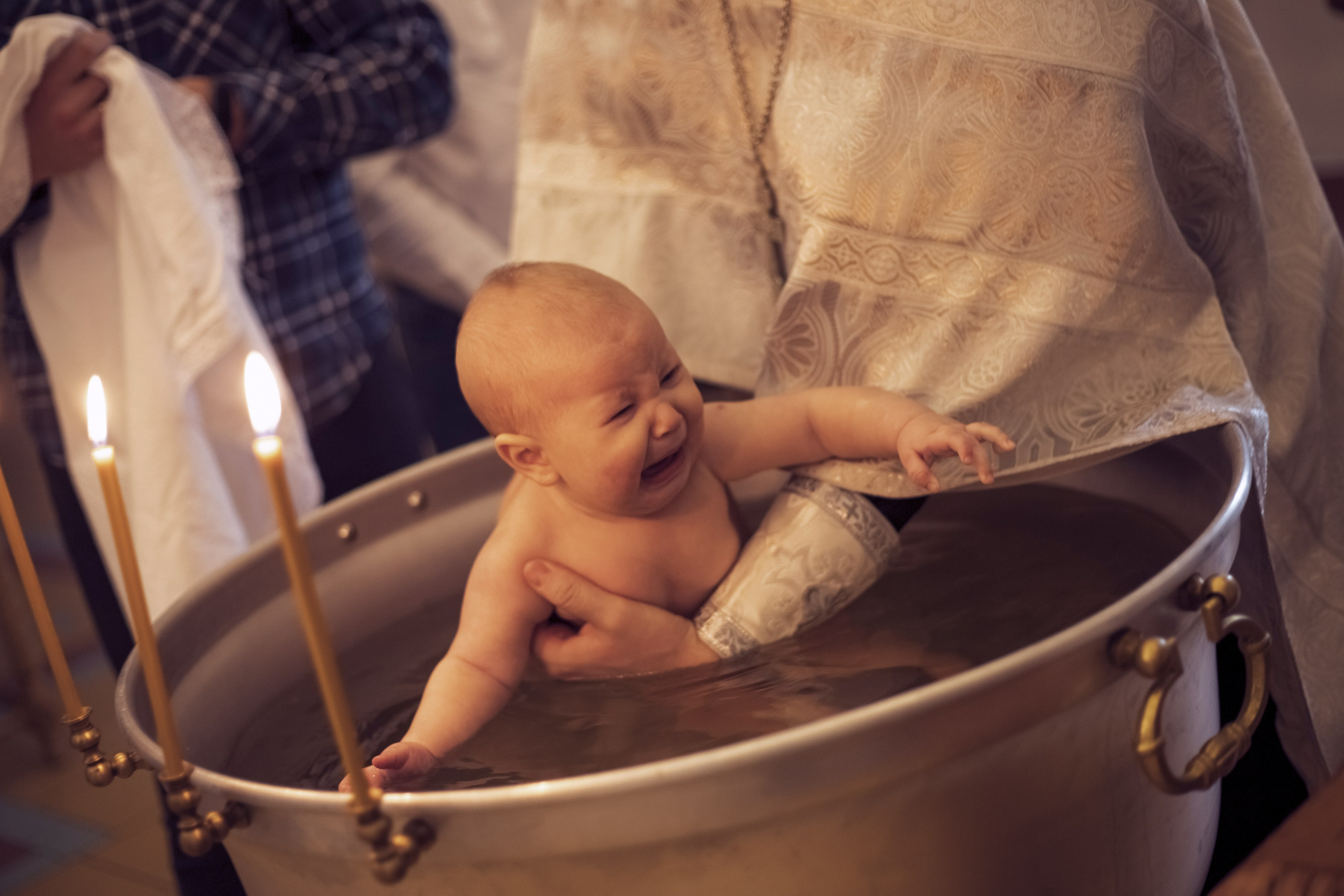 батюшка опускает в чан с водой ребенка