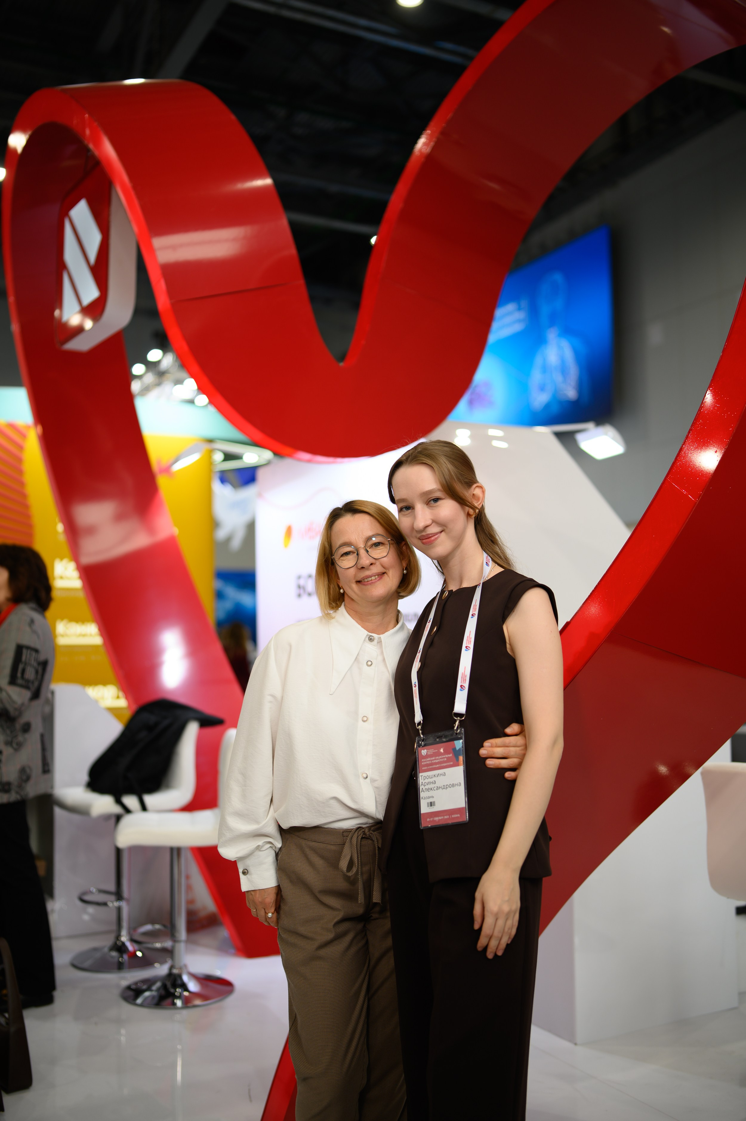 Женщины в корпоративной форме позируют у стойки медицинской компании на конгрессе кардиологов, репортажная фотосъемка от фотографа Алексея Клейменова, Казань