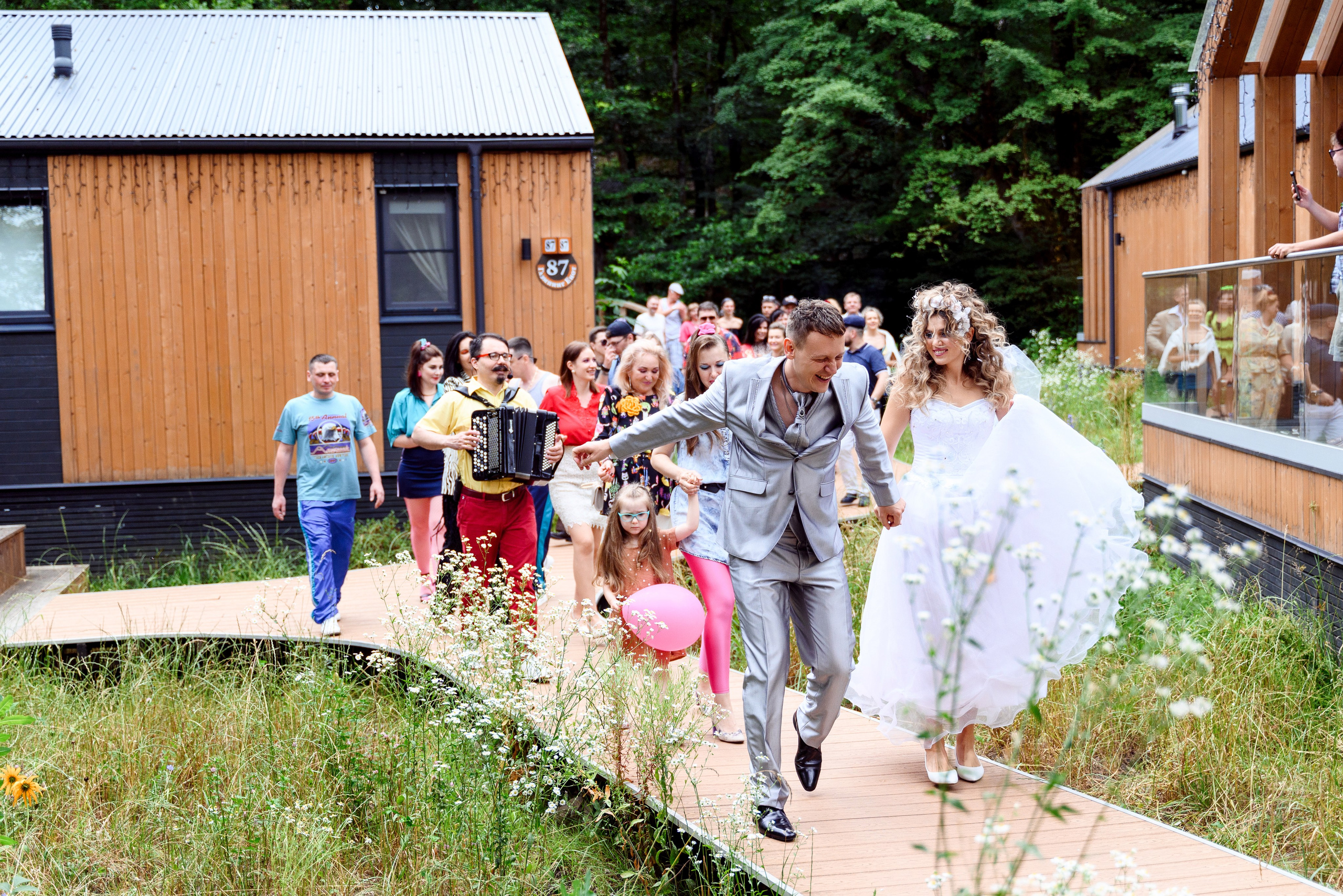 Гости танцуют и смеются, создавая атмосферу веселья жених невестой идут впереди держась за руки 