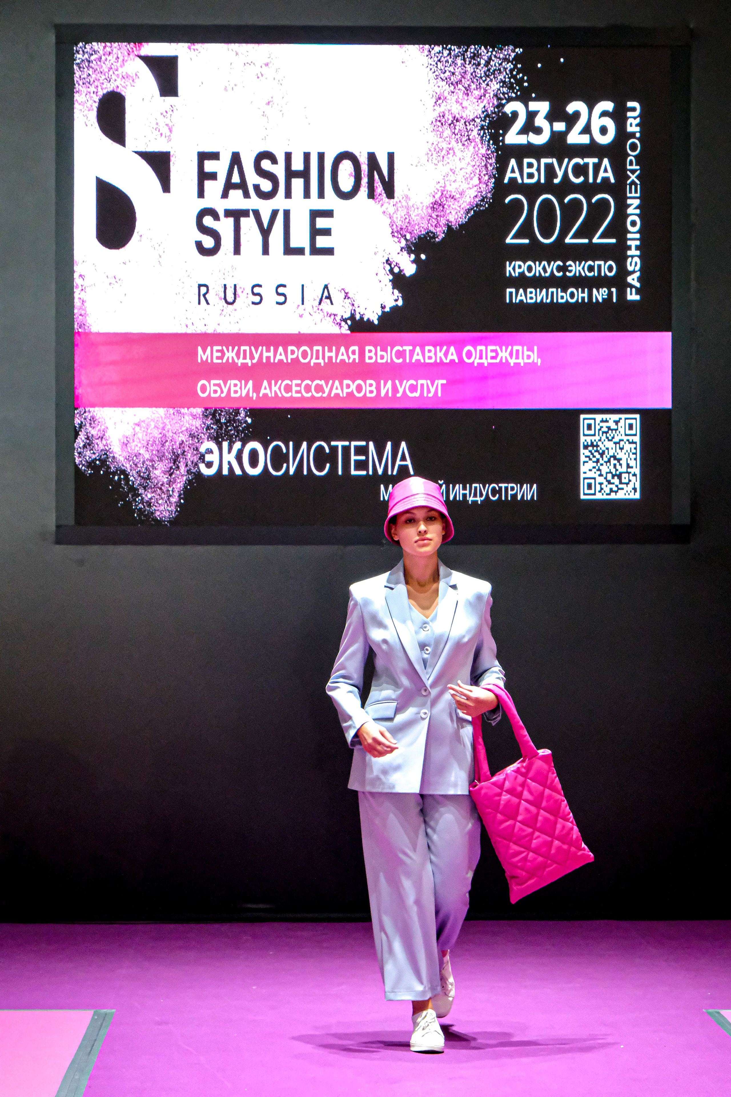  "Модели в ярких нарядах проходят по подиуму во время показа мод, освещенные яркими софитами и окруженные восторженными зрителями."