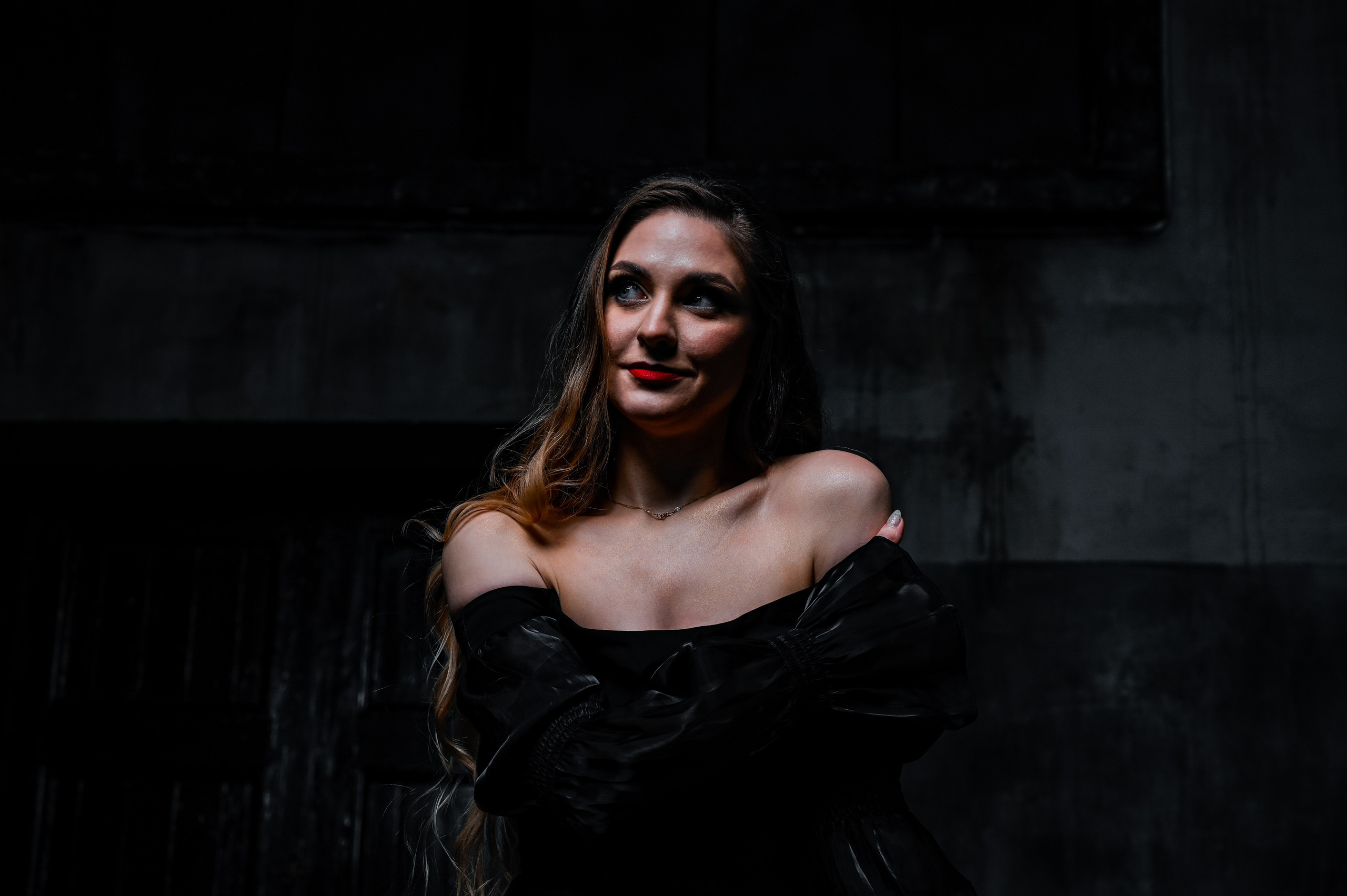 Эмоциональный женский портрет в стиле нуар с естественным освещением. Фотография выделяет глубину взгляда и уверенность молодой женщины с длинными волнистыми волосами, одетой в элегантное чёрное платье с открытыми плечами. Идеально для профессиональной фотосессии, личного блога, соцсетей или рекламных кампаний. Студийная съёмка с акцентом на естественную красоту и стиль. Ключевые слова: женский портрет, профессиональная фотография, студийная съёмка, естественное освещение.