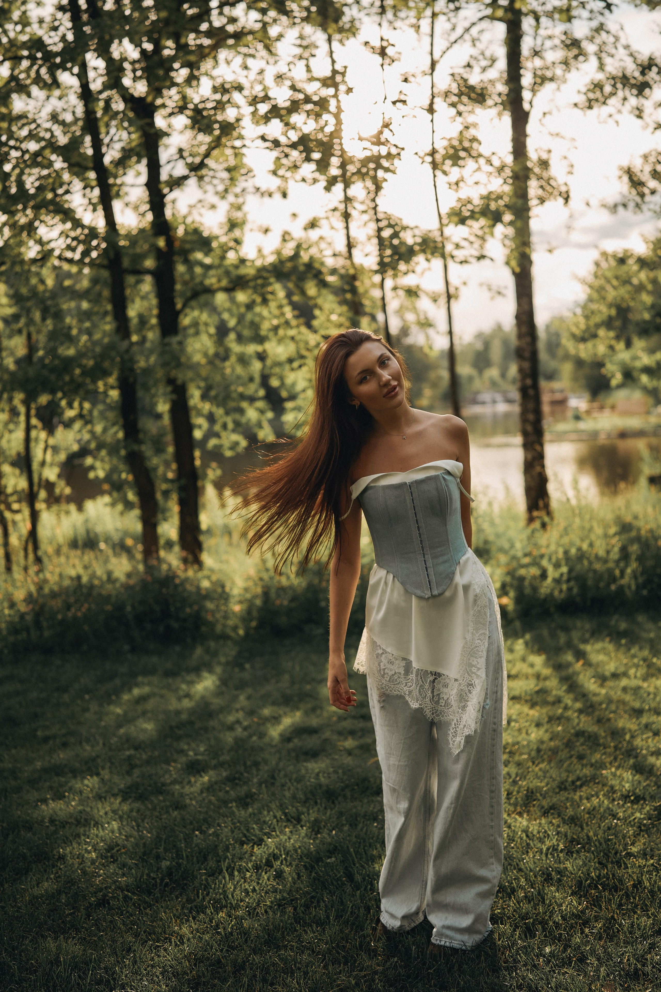 Женская фотосессия на природе в лесу, девушка в белом платье стоит среди деревьев в мягком солнечном свете
