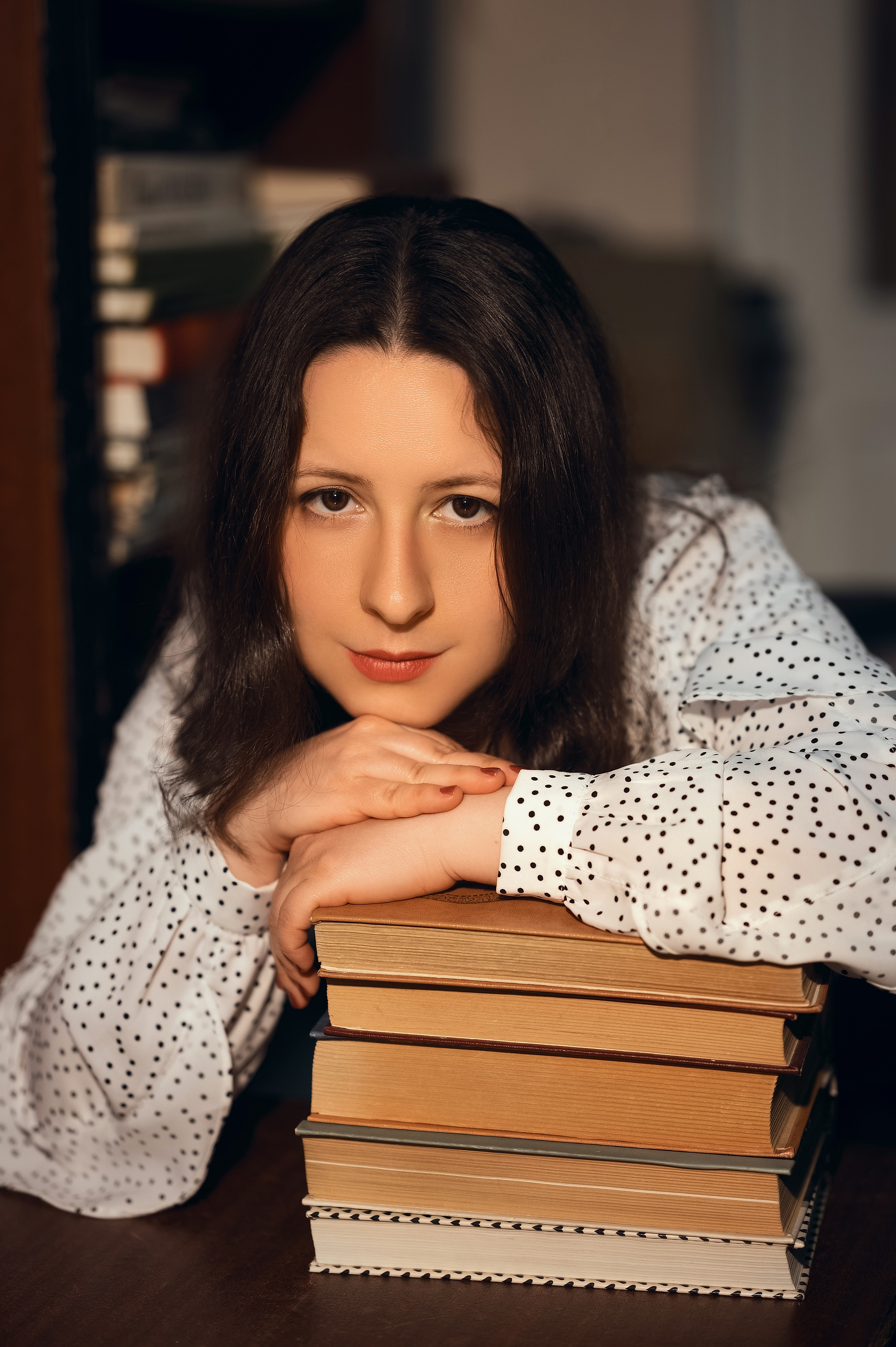 Фотосессия в Центральной библиотеке Волгодонска. Девушка в светлой блузке и тёмной юбке читает книгу среди стеллажей. Фотограф — Елизавета Жуйкова.