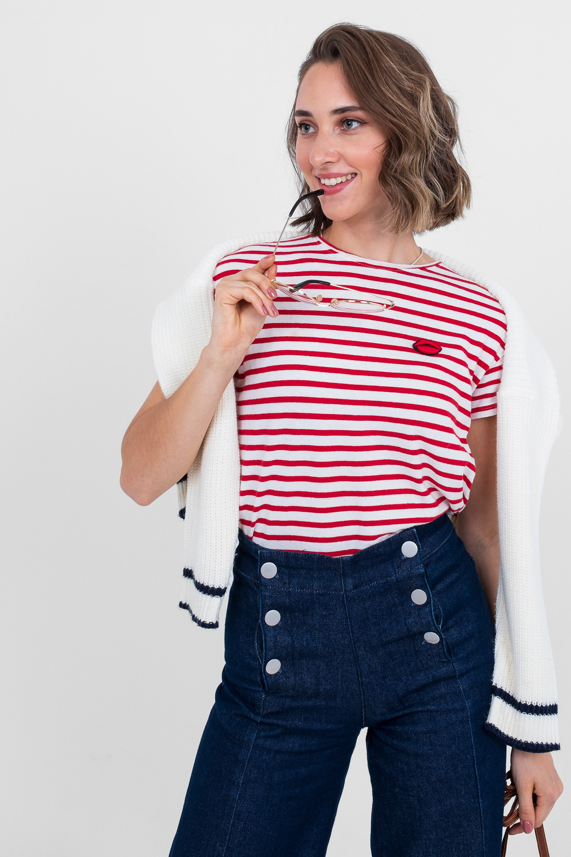 На изображении девушка в очках в полосатой футболке с белой кофтой и широких джинсах с пуговицами.  Фото для маркетплейсов