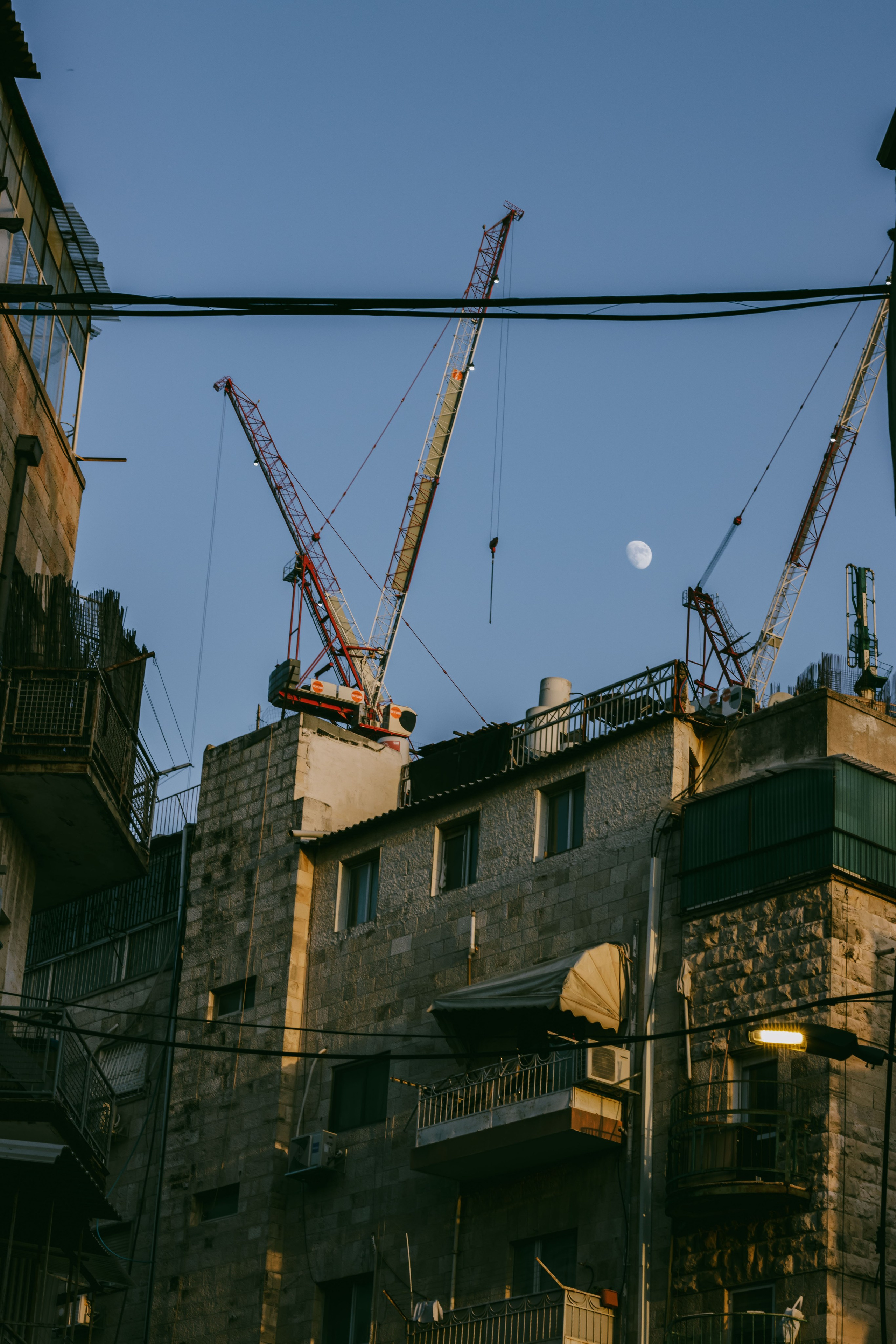 башенные краны на фоне каменных домов и большой луны