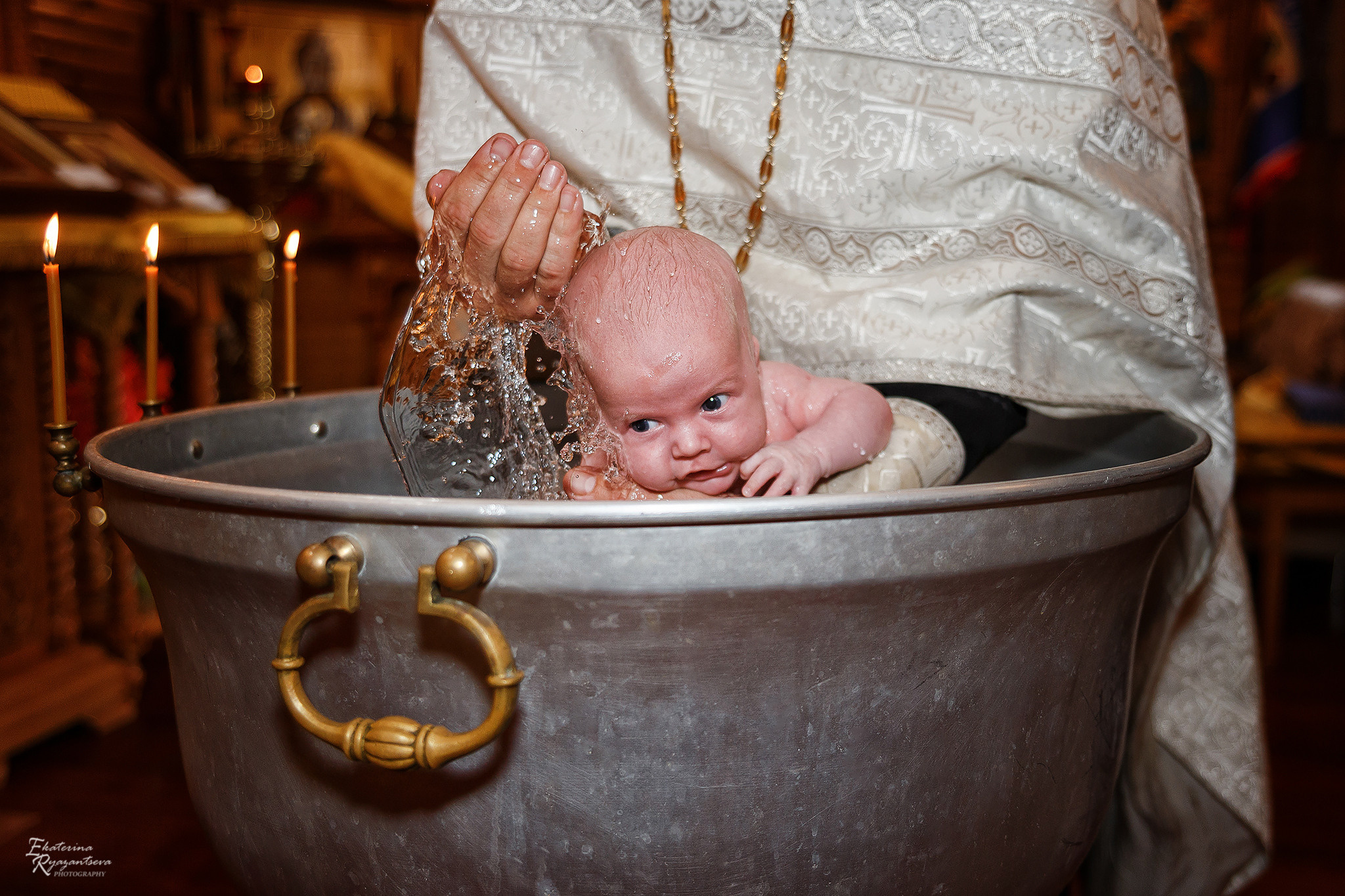 батюшка окунает малыша в купели