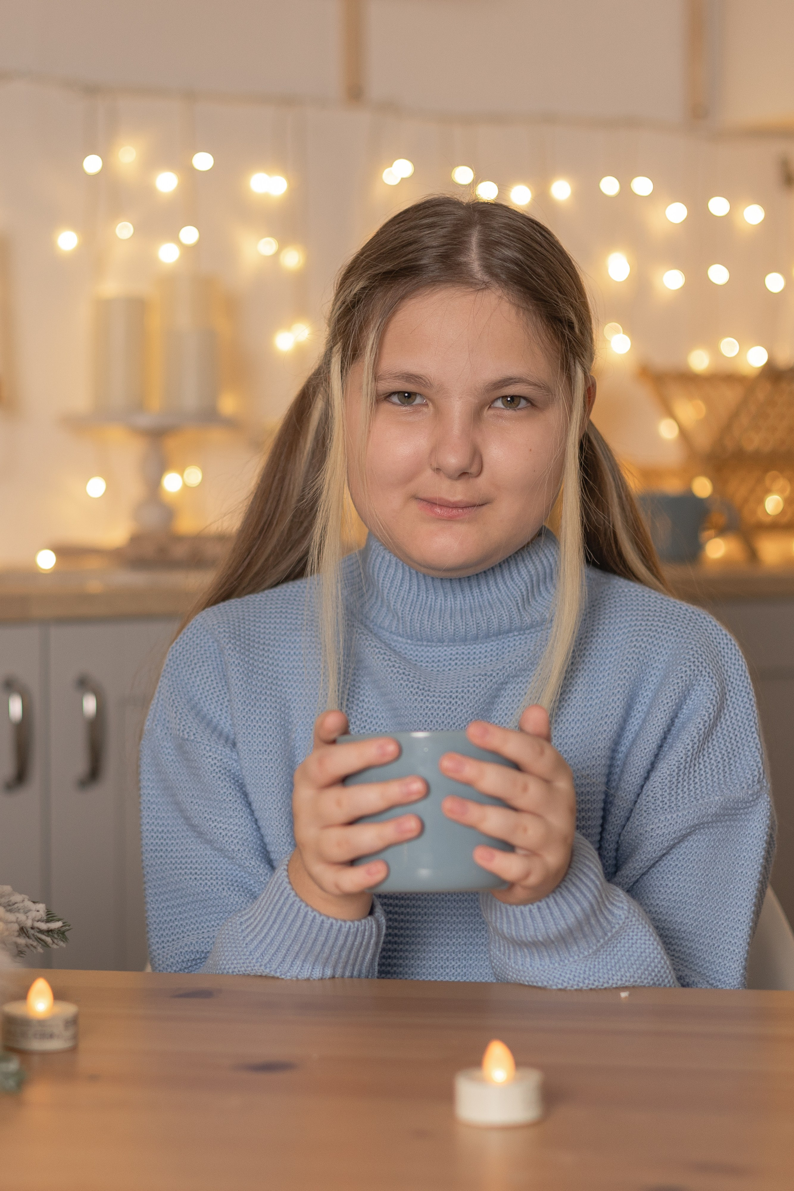 Девушка сидит за столом держит кружку в руках