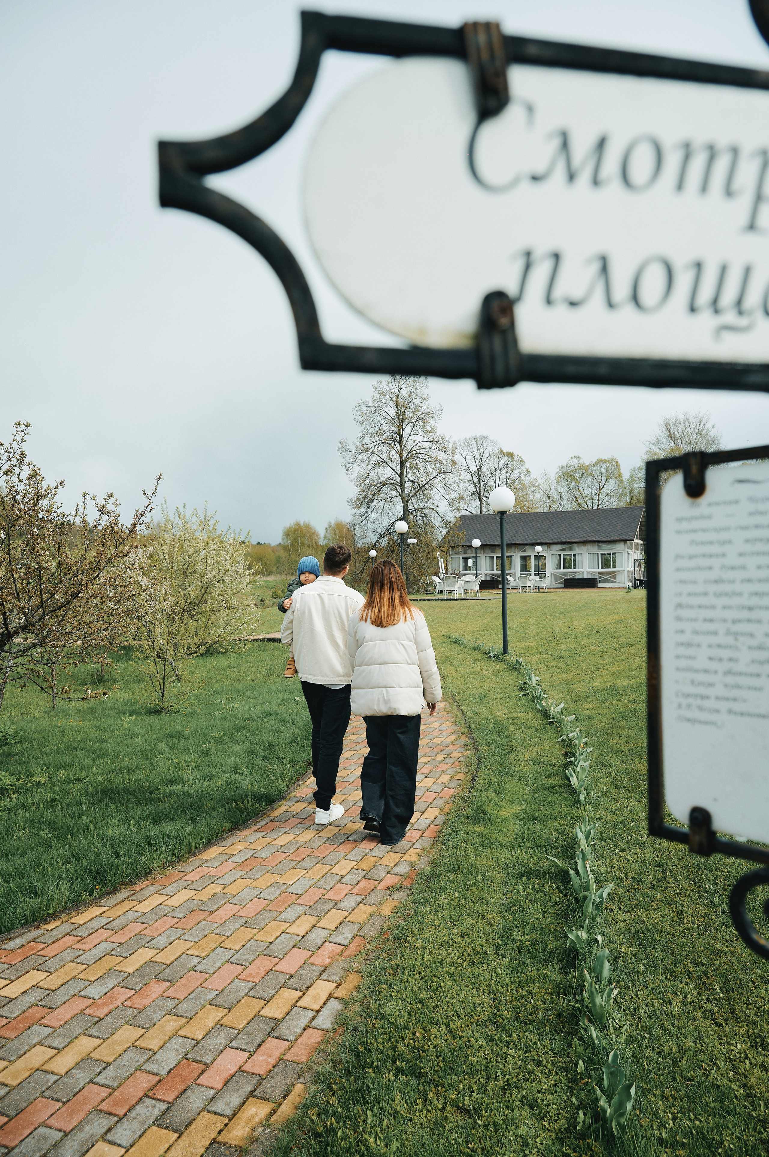 семья идёт по аллее к загородному дому весной, вид со спины, указатель "Смотровая площадка