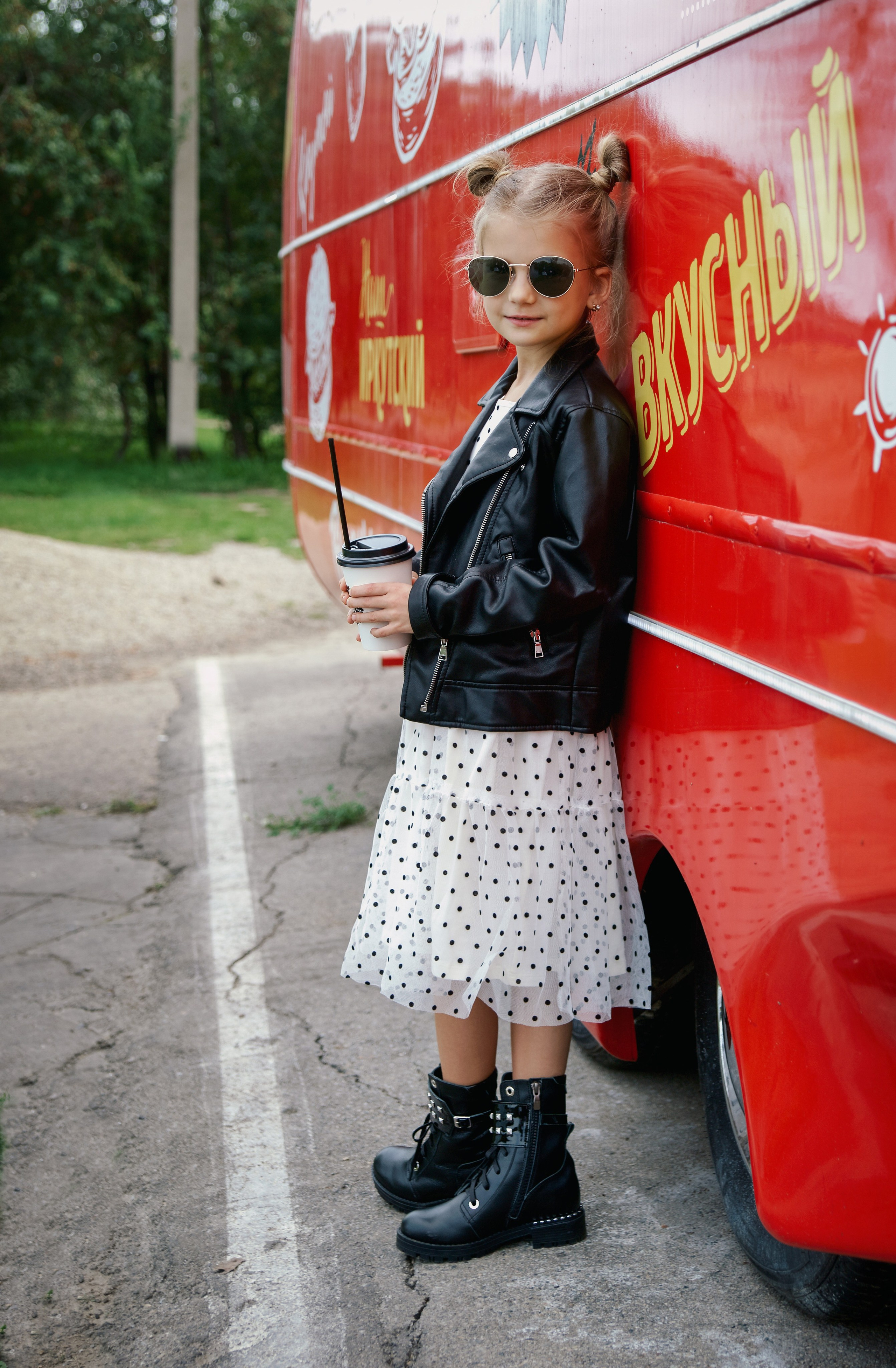 Детская фотосессия летом - девочка стоя в кожаной куртке и черных очках