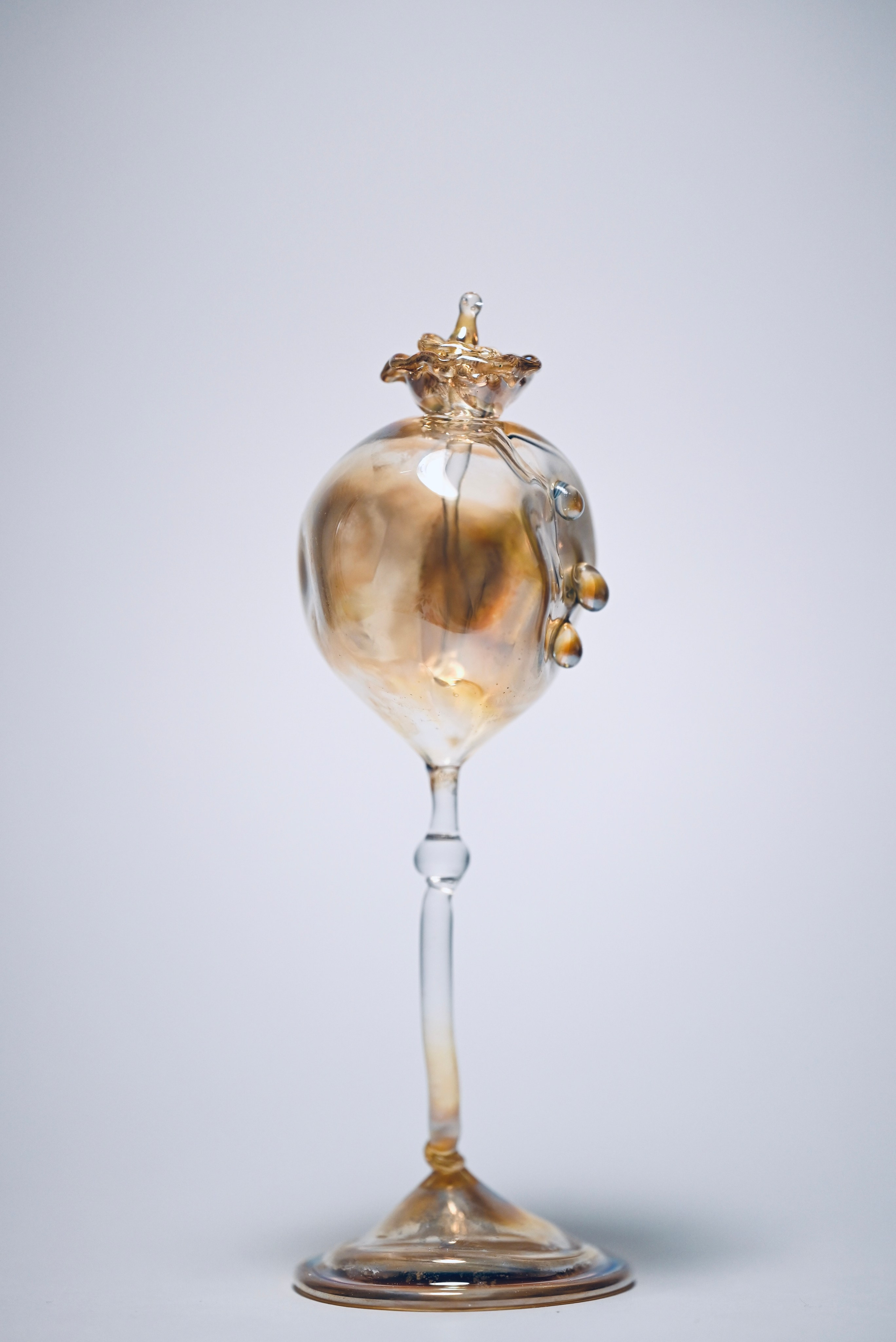 "Seed Pod." 15x5 cm. Lampworking, borosilicate glass, silver and gold fuming. 2025.A vessel referring to the culture of poppy and opium as substances that are simultaneously ritualistic and prohibited. The work addresses Eastern traditions in which the sacred and the taboo coexisted for a long time within a single material gesture.