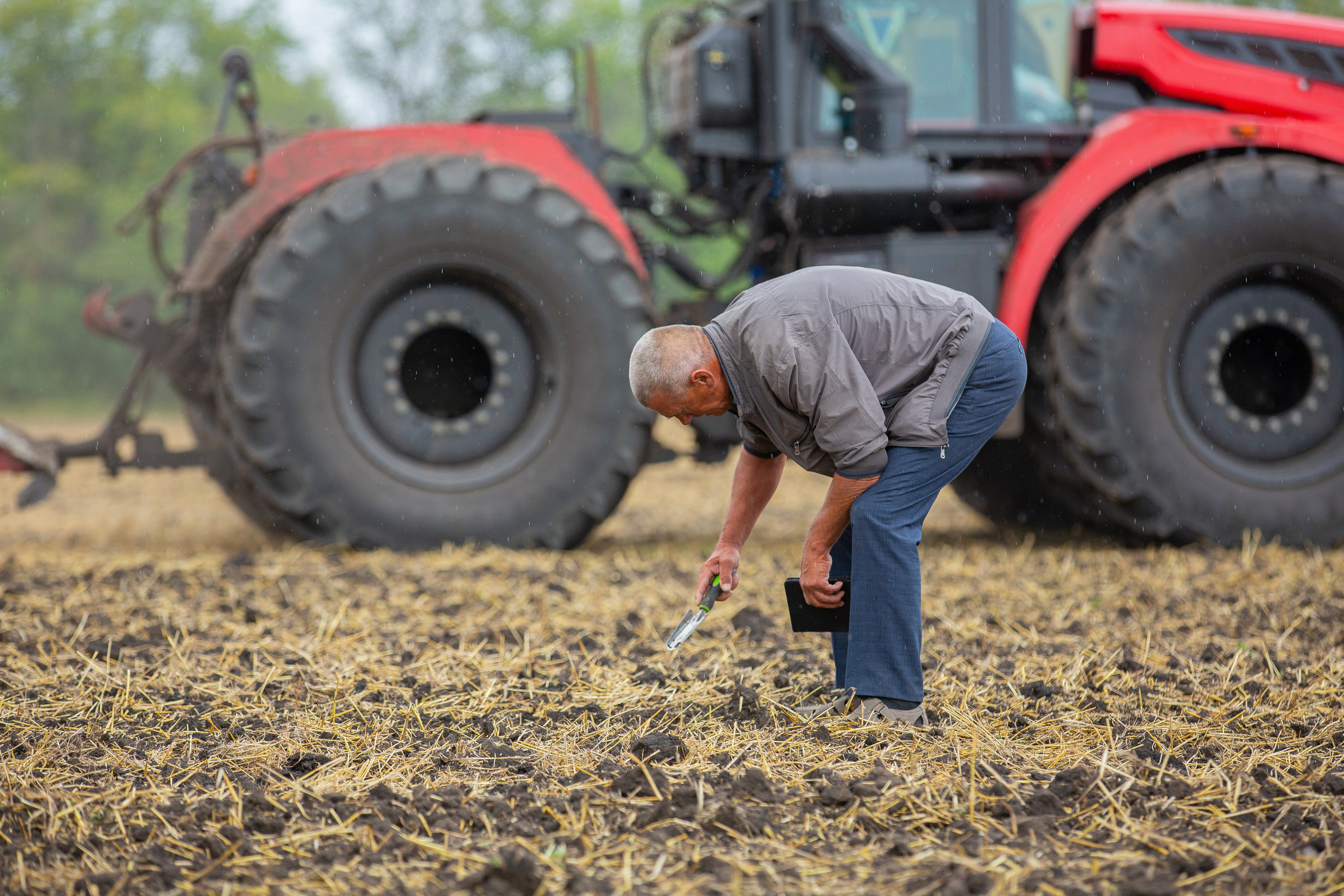 Агроном на фоне трактора Кировец проводить пробу пашни