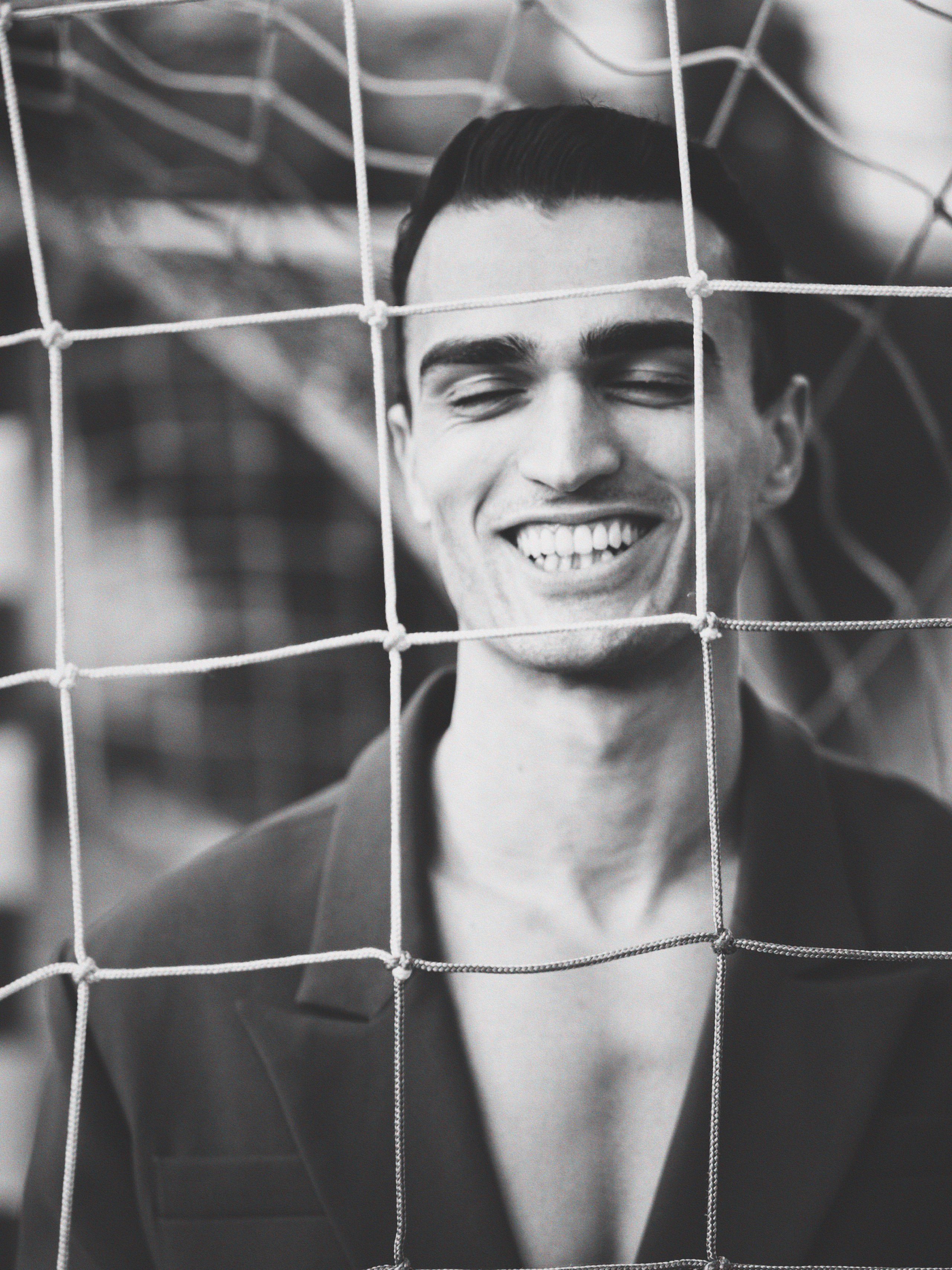 Black and white fashion portrait of male model behind net, expressive editorial photography, Sergio Maiis