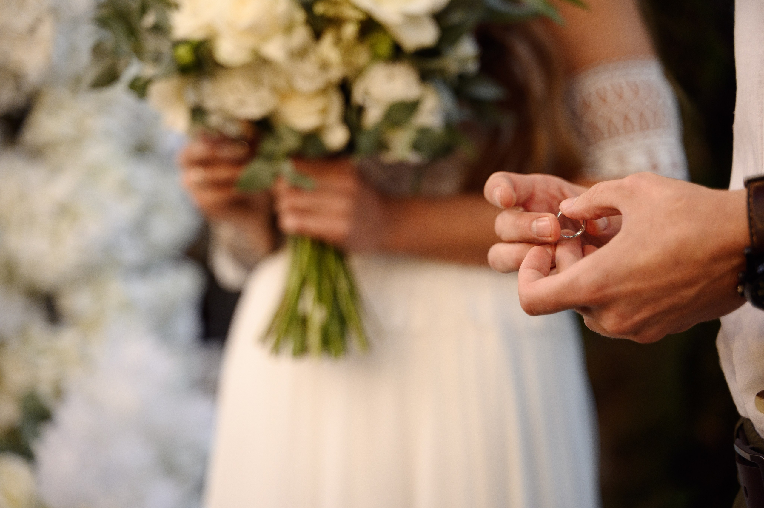 Крупный кадр как жених держит кольцо в руке которое собирается надеть на палец невесте