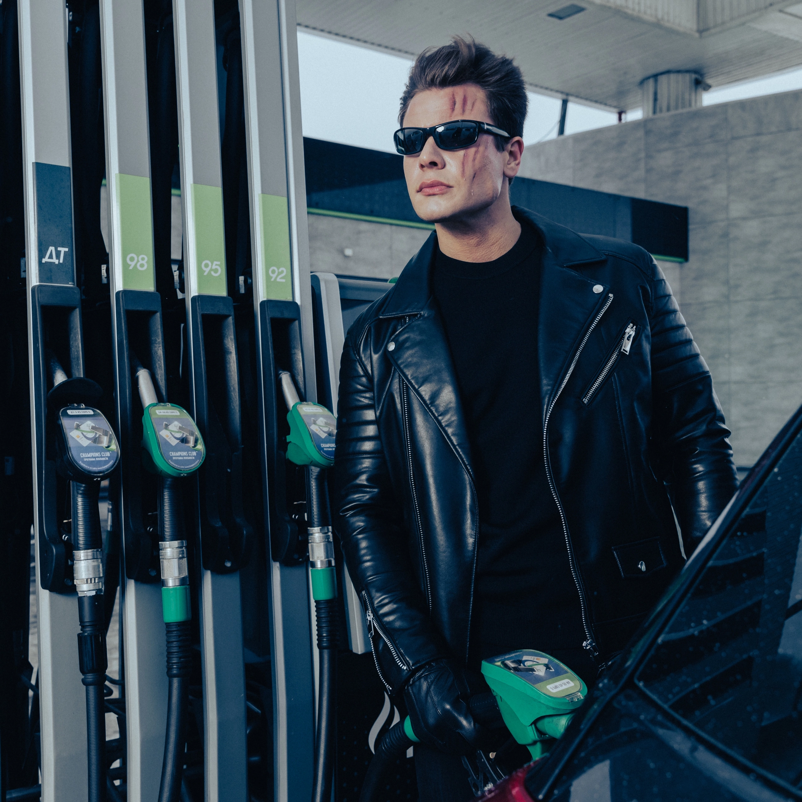 Мужчина модель в кожаной куртке на заправляет машину бензином на заправке