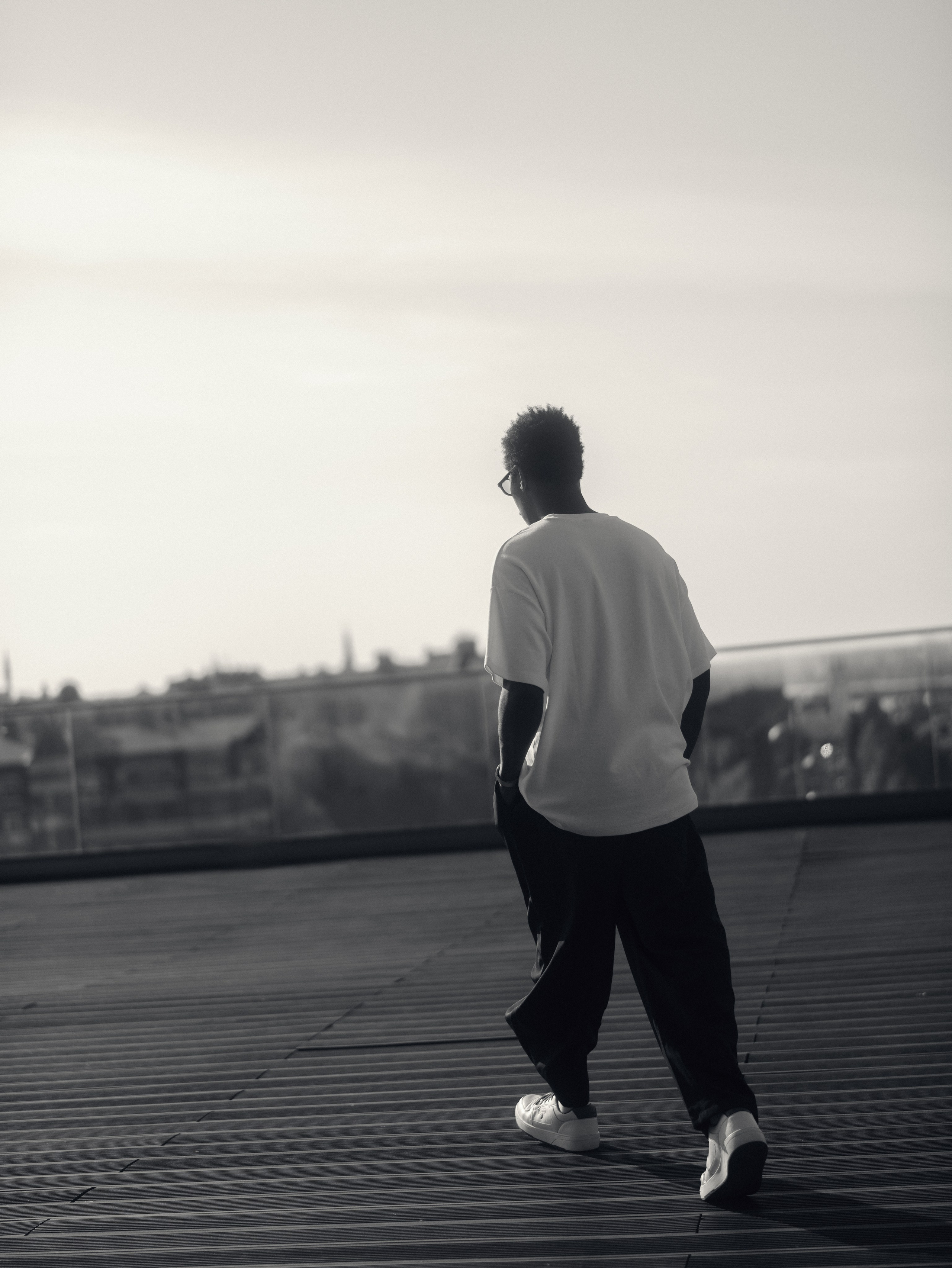 Азиз удаляется по деревянному настилу смотровой площадки в Казани на фоне светлого неба.
