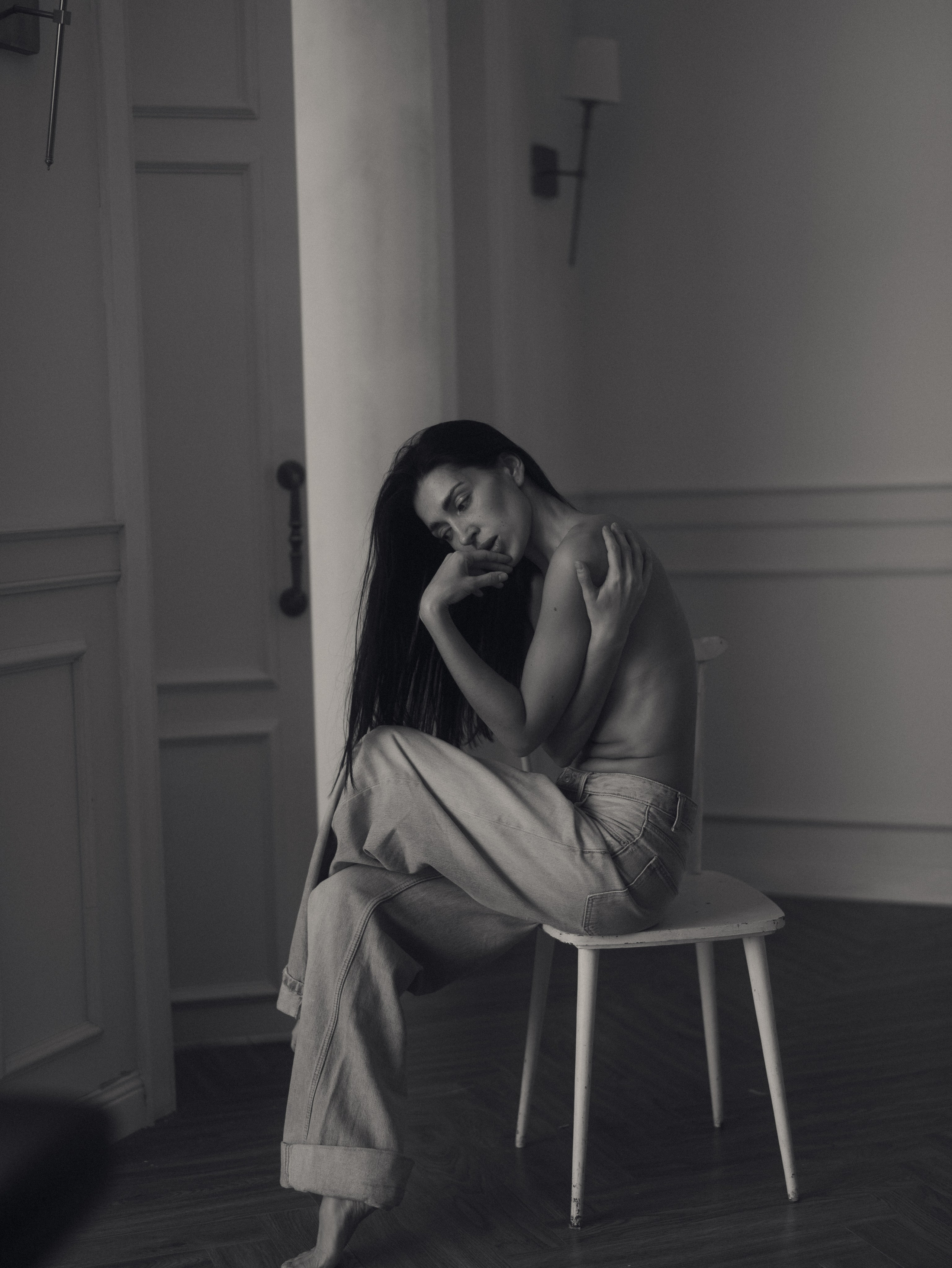 Камилла сидит на белом стуле в зале фотопространства на чёрно-белом кадре.