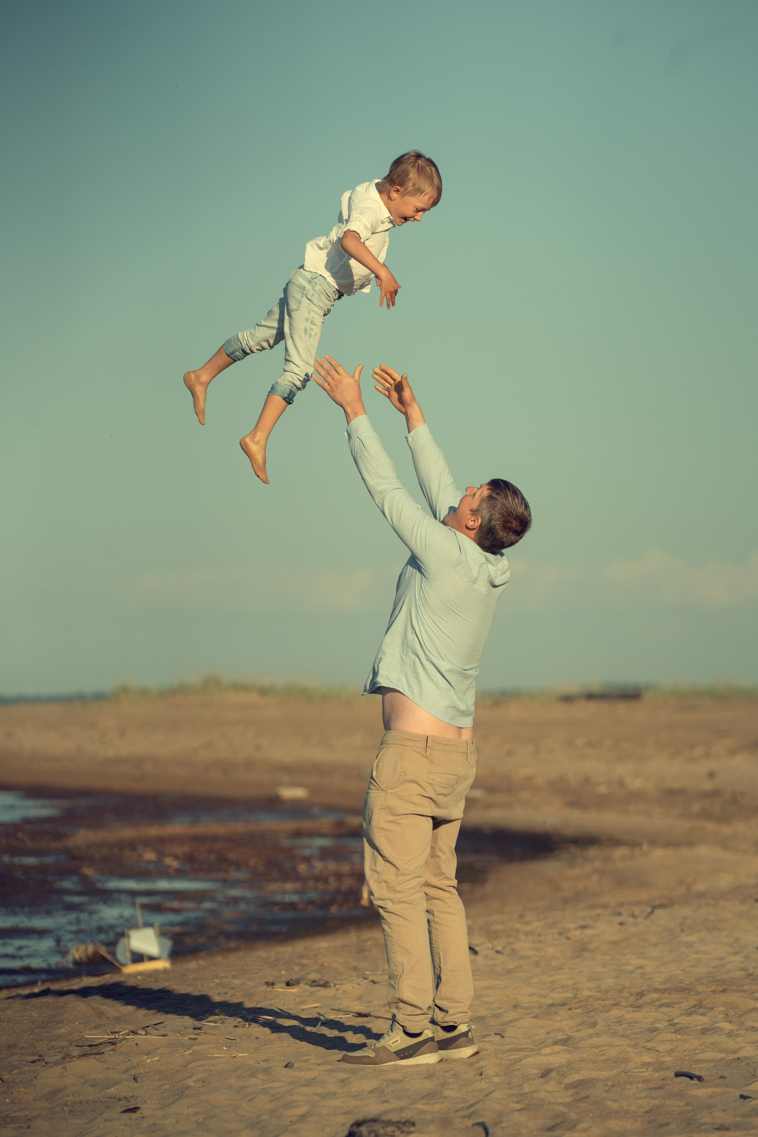 Папа играет с ребенком, подбрасывая его и ловя. Мальчик очень счастлив. Игра на берегу моря .