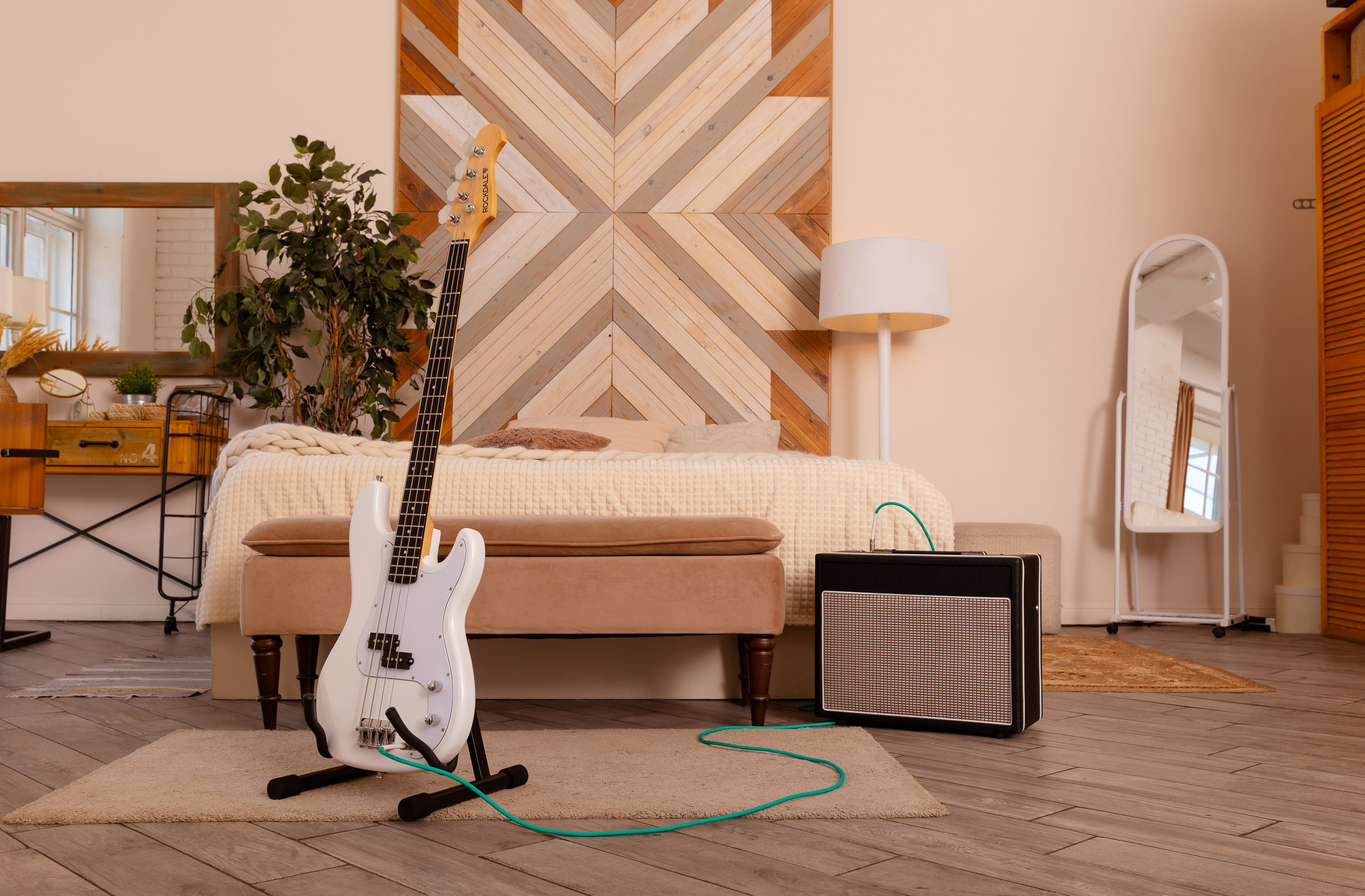 Белая гитара стоит на подставке, на фоне меблированной комнаты.