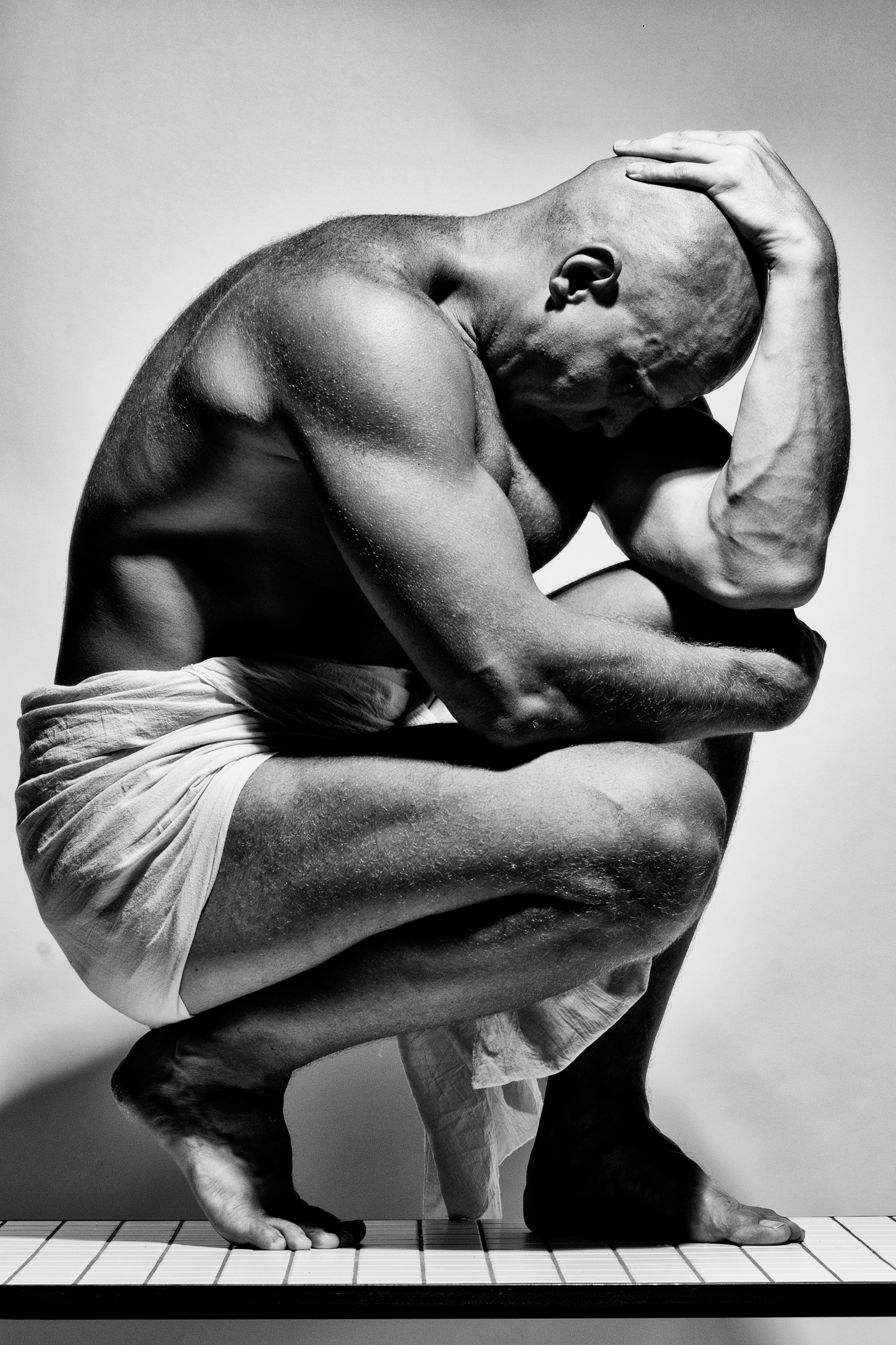 мужчина в драпировке сидит на столе на корточках рука лежит на голове 