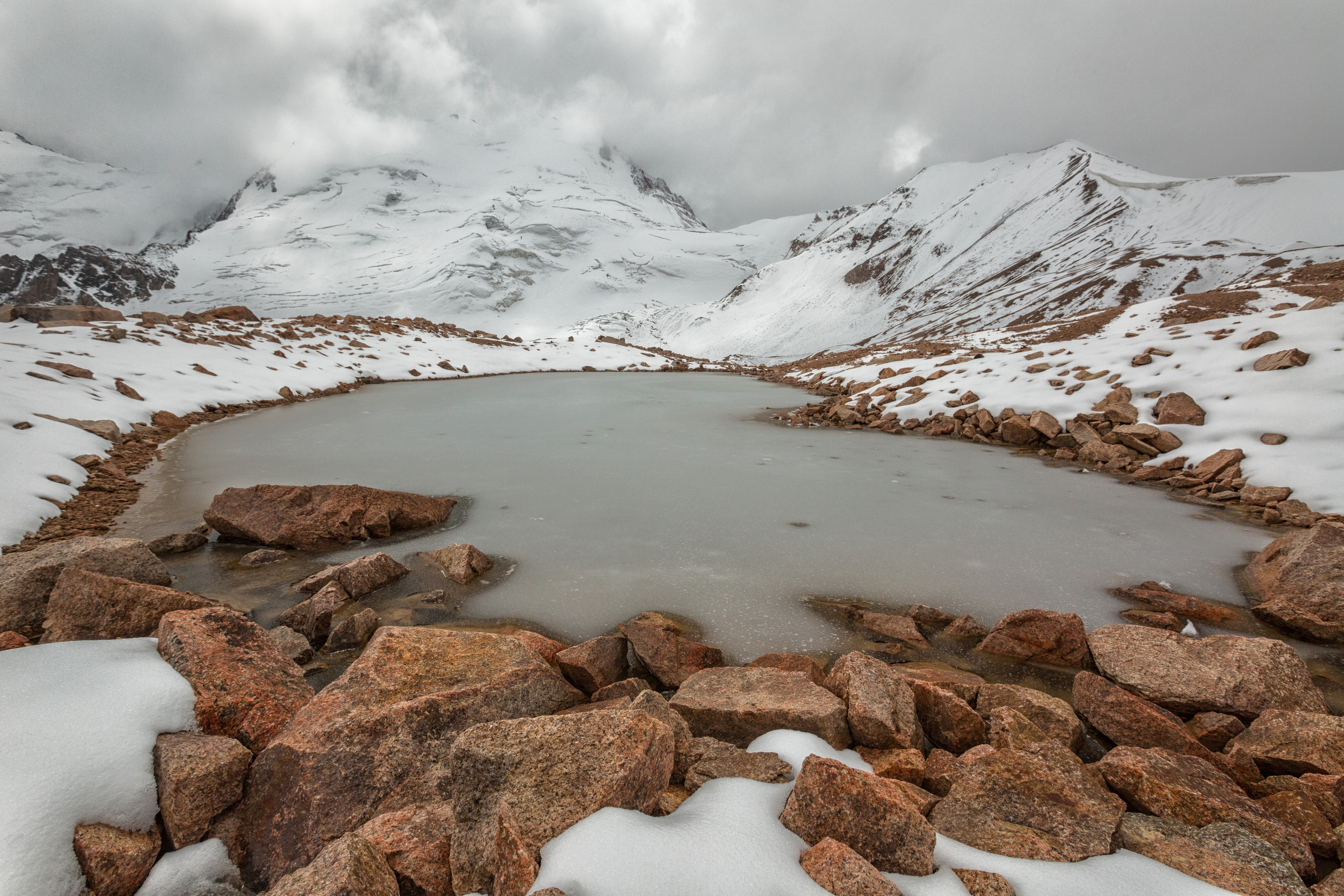 Маленькое, покрытое льдом озеро в горах в окружении кучевых облаков