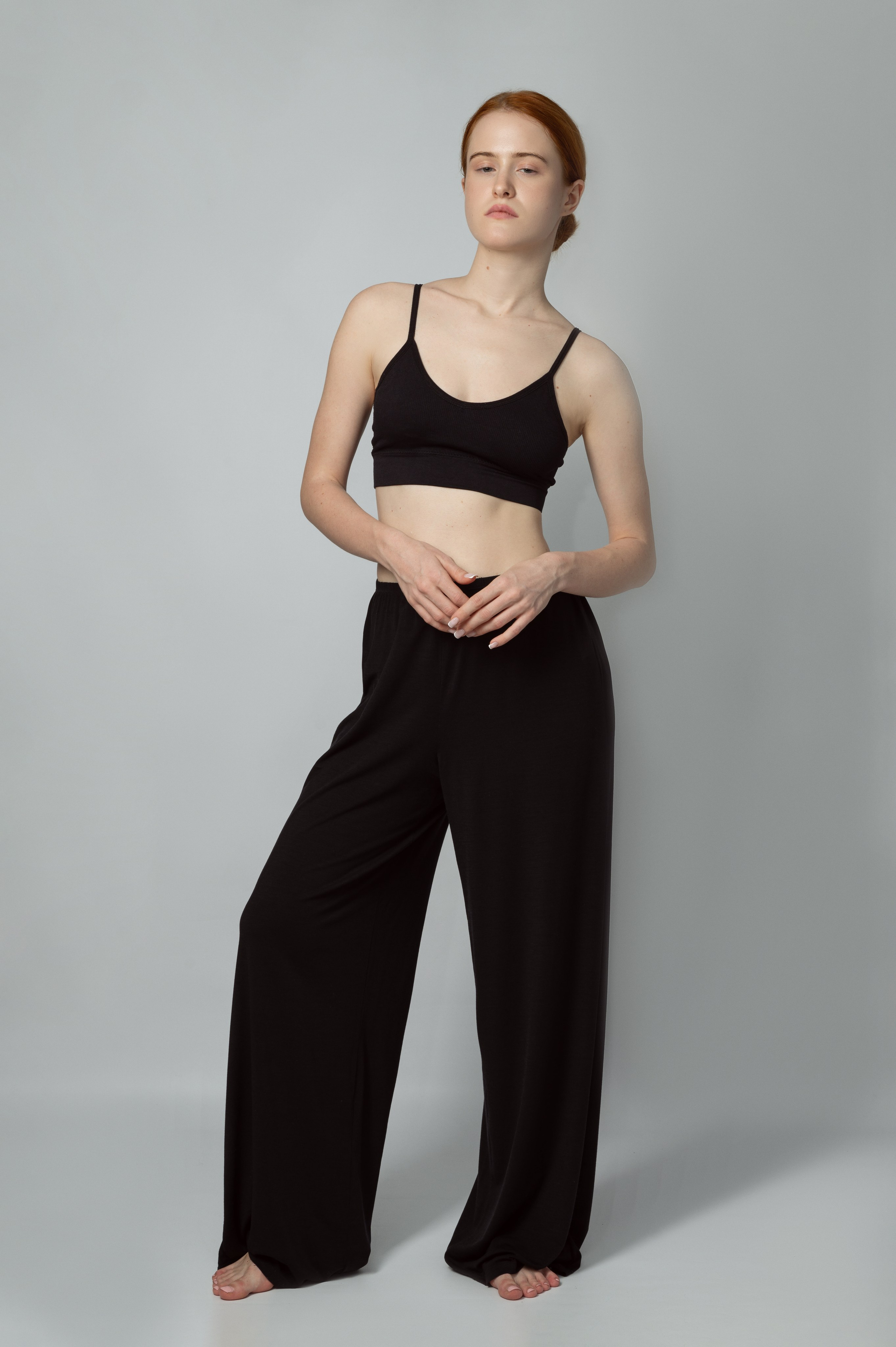 Рыжеволосая девушка-модель в черном топе и черных брюках на сером фоне. Модельные тесты