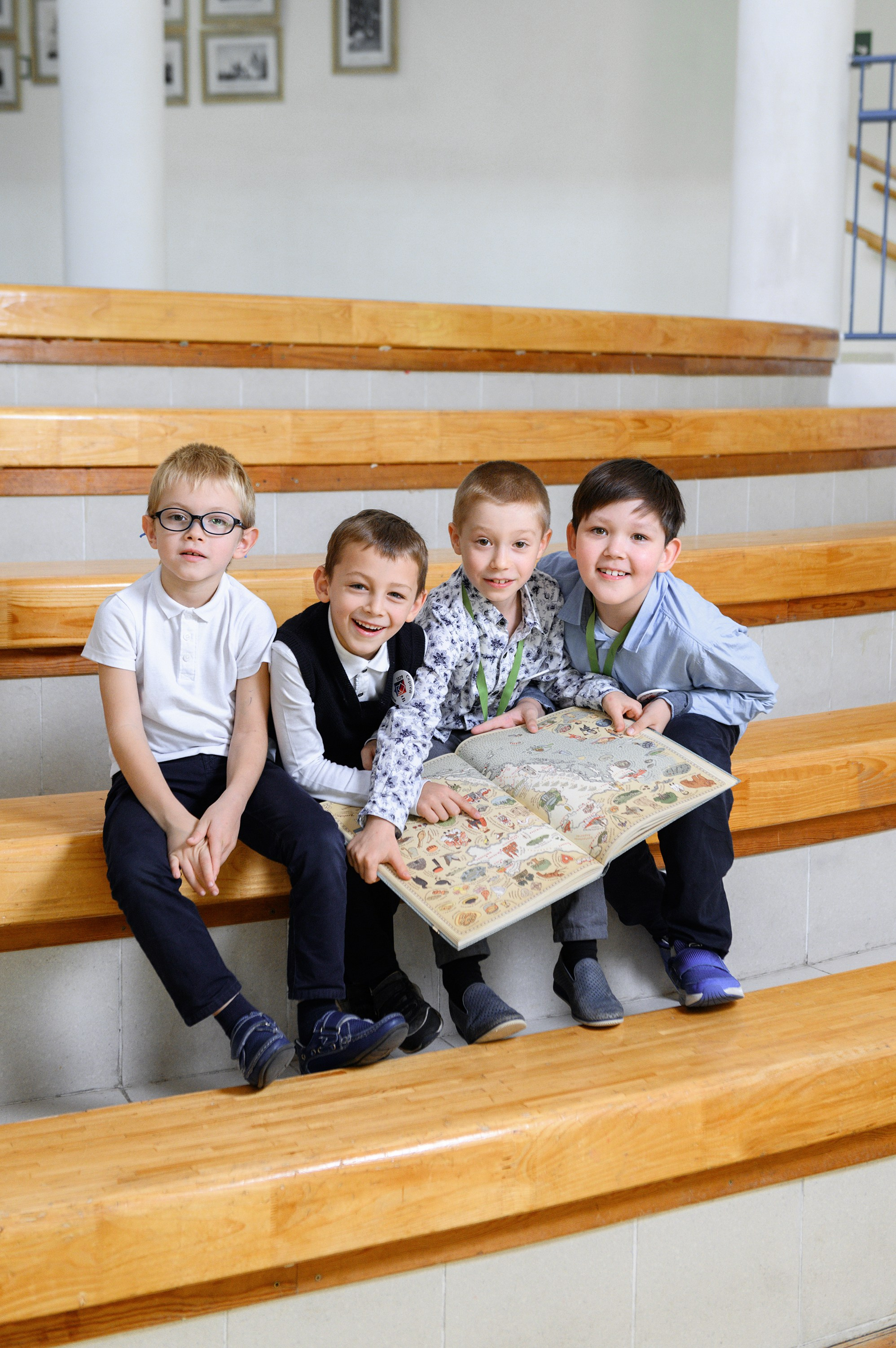 Группа учеников сидит на трибунах в школьном коридоре