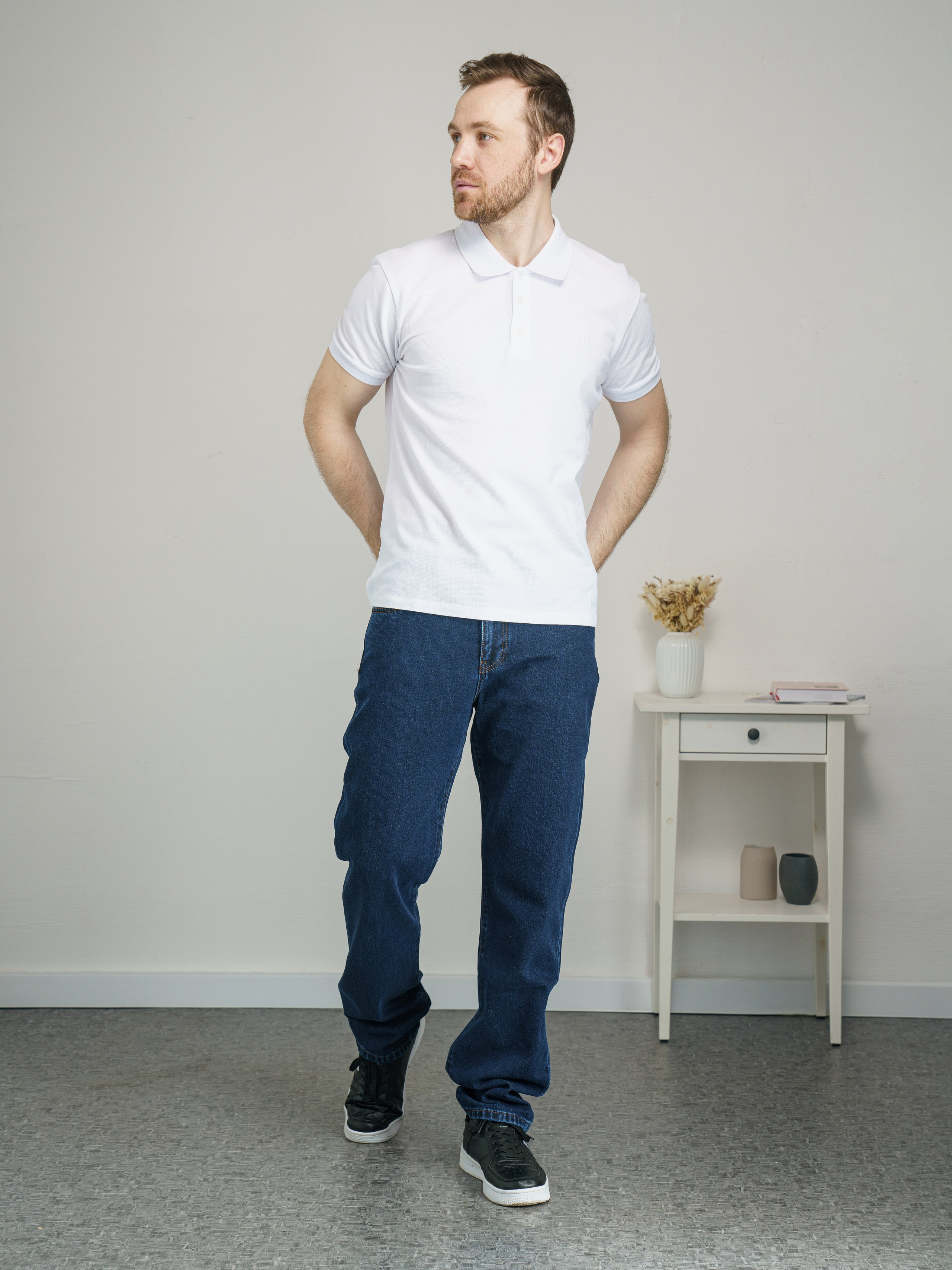 Мужчина с короткой щетиной в белом поло и синих джинсах