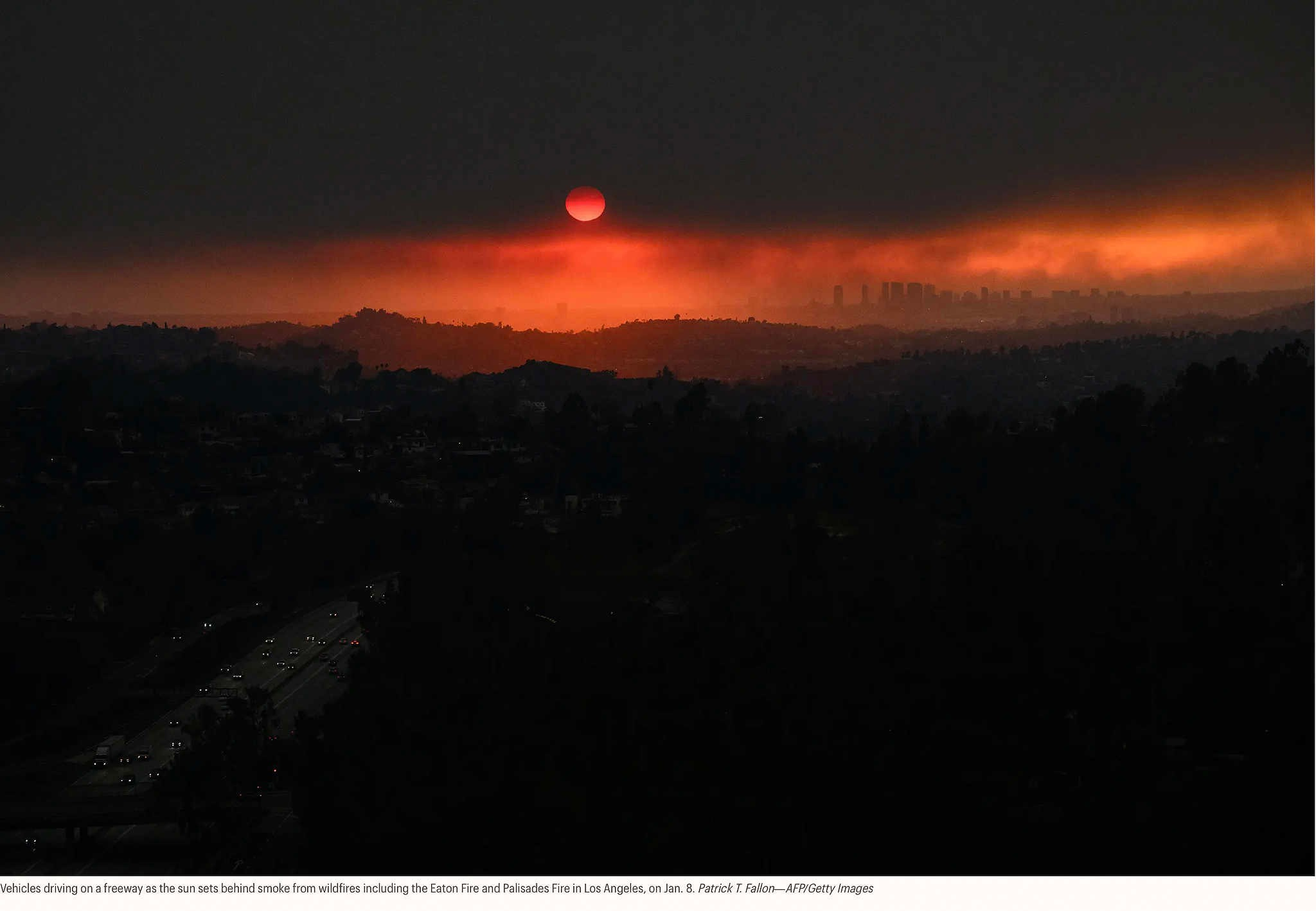 Автомобили едут по автостраде, а солнце садится за дымом от лесных пожаров, в том числе от пожаров Итон и Палисейдс в Лос-Анджелесе, 8 января. Патрик Т. Фэллон — AFP/Getty Images
