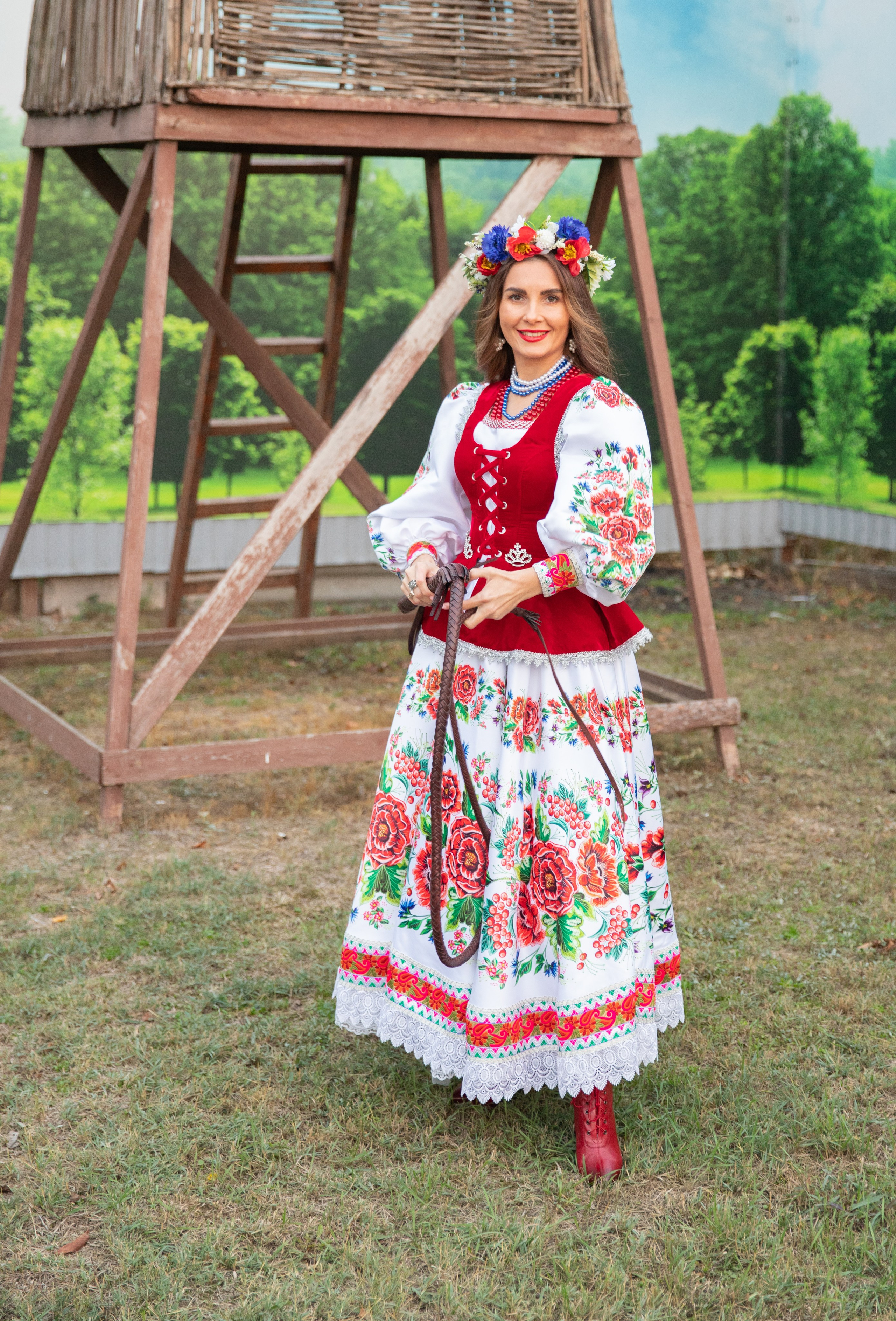 Молодая девушка в шикарном казачьем наряде позирует на фоне живописного хутора, создавая атмосферу традиционной культуры.