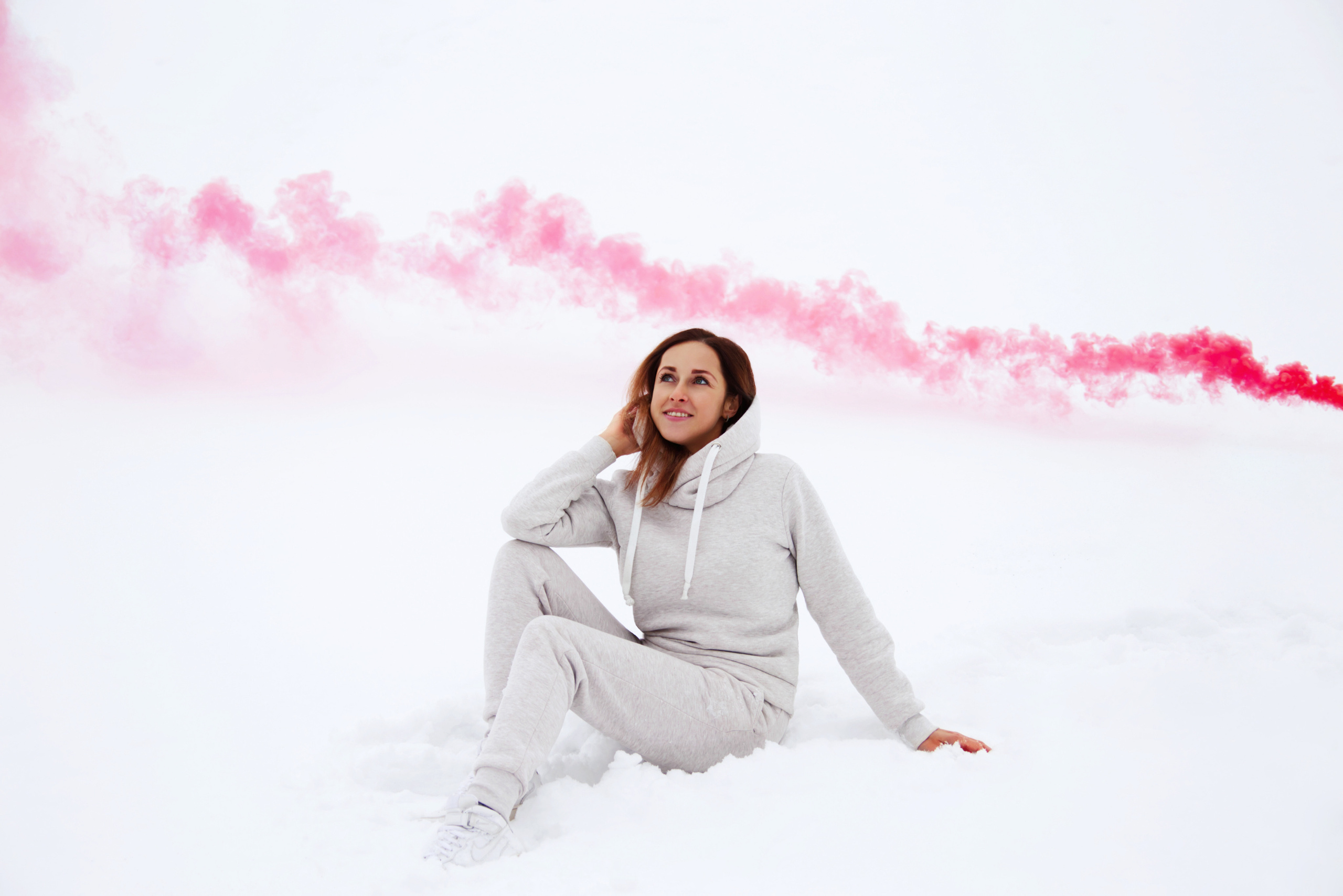 Девушка сидит на снегу на фоне цветного дыма зимой
