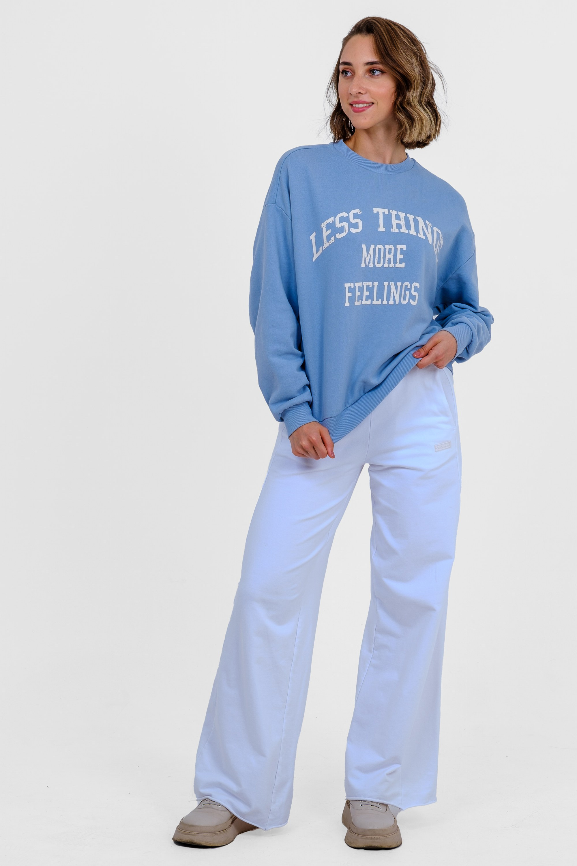 Девушка в голубом свитшоте с принтом, голубых спортивных брюках и белых кроссовках. Вид спереди. Фото для маркетплейсов