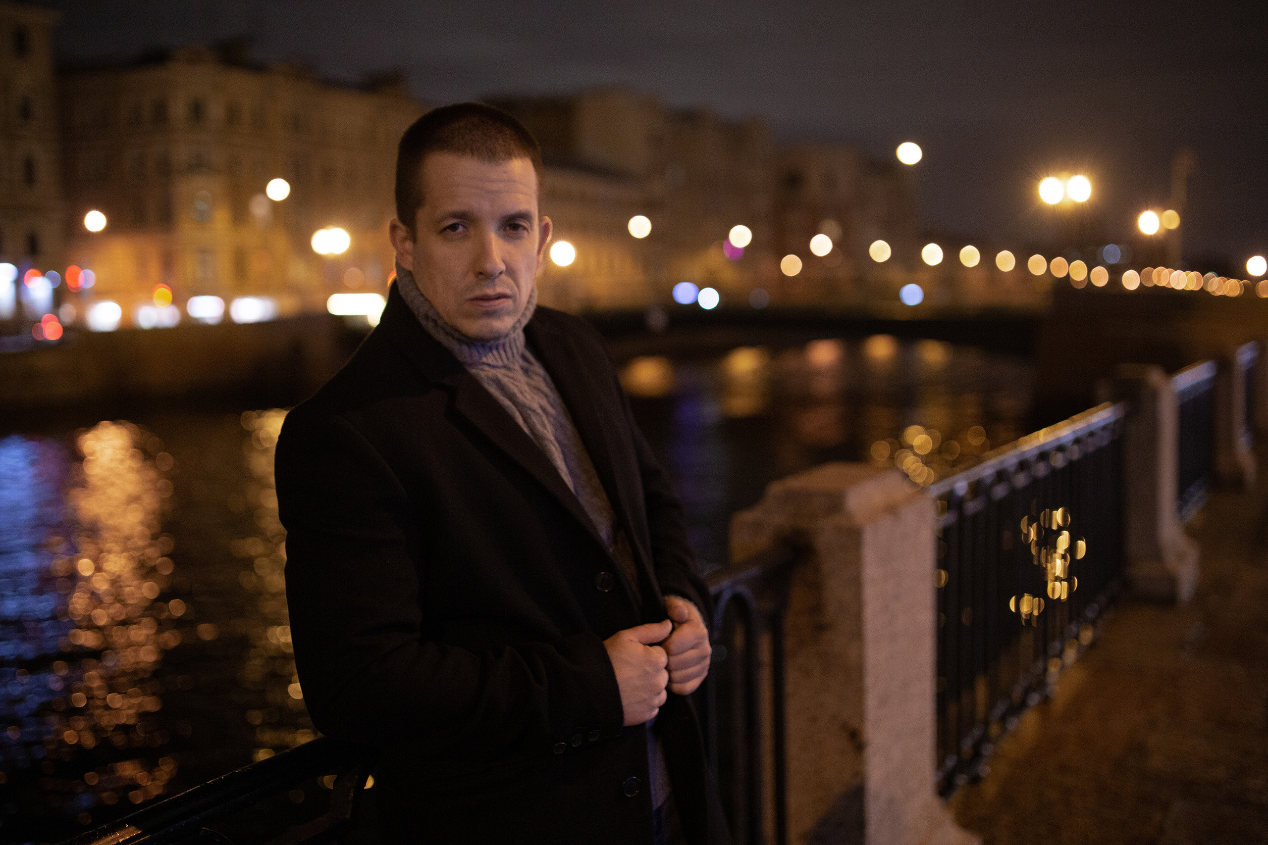 Парень в пальто на набережной реки вечером в Санкт-Петербурге.