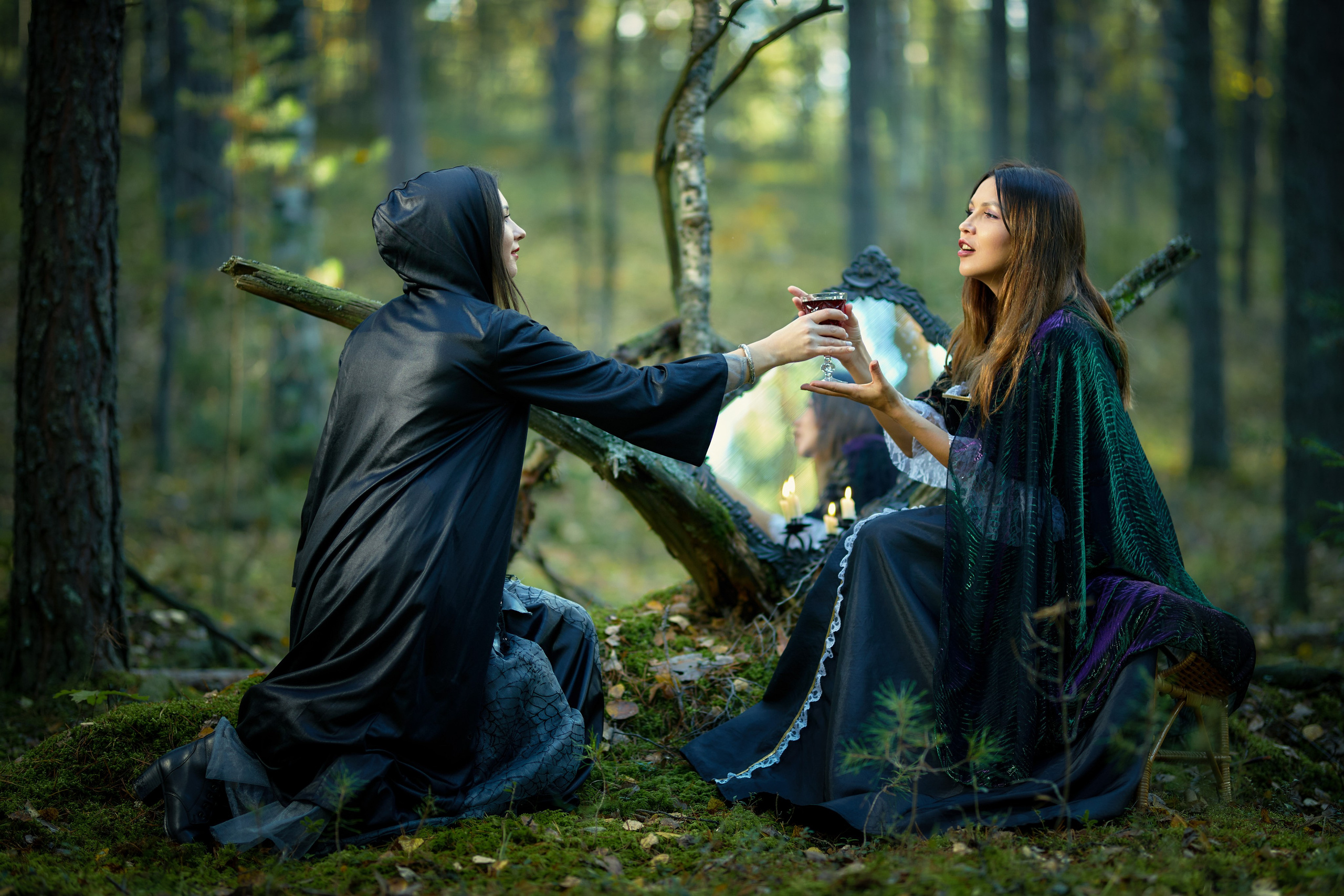 Одна ведьма подает бокал с вином второй в лесу у колдовского зеркала