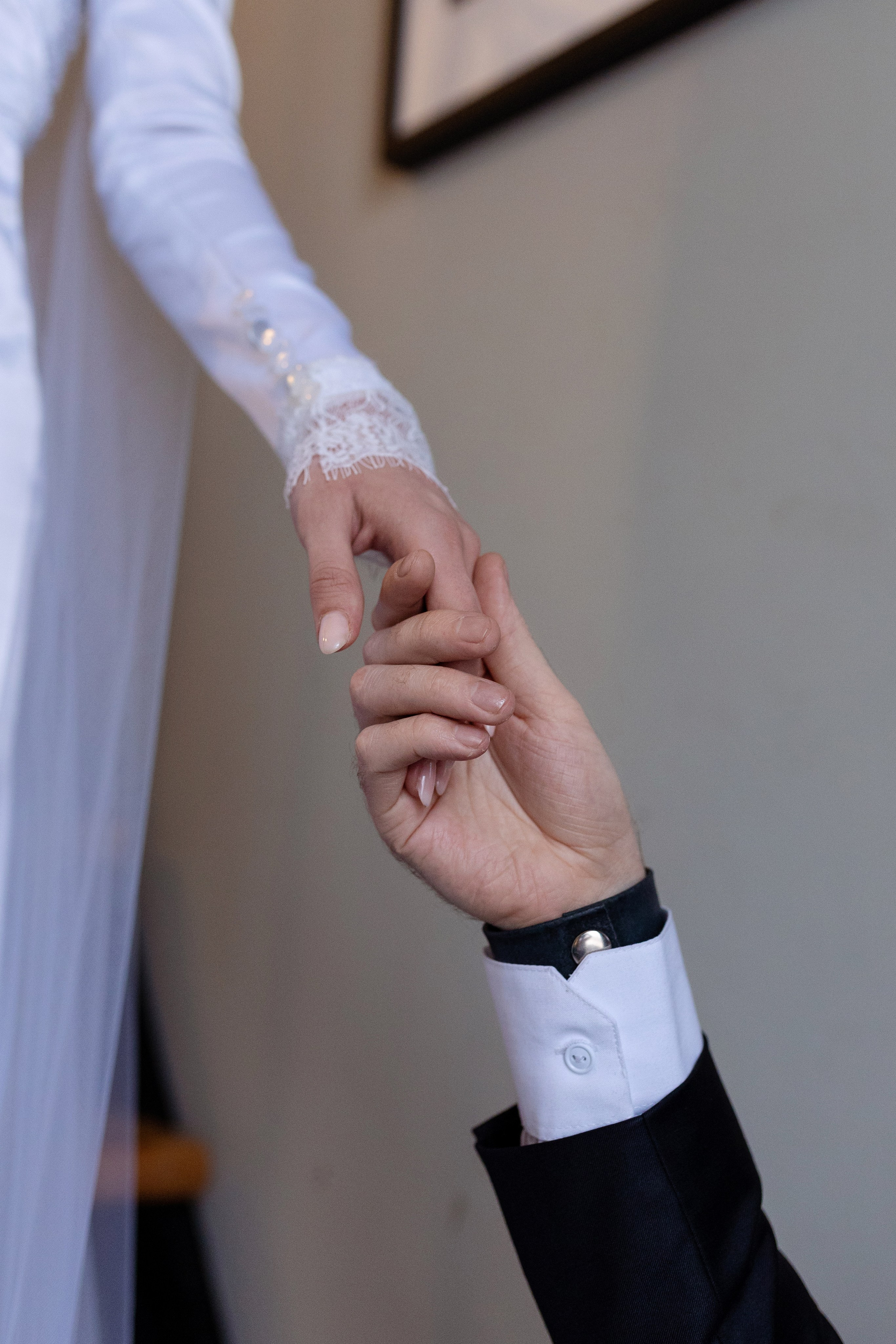 Рука жениха нежно держит руку невесты на сером фоне.