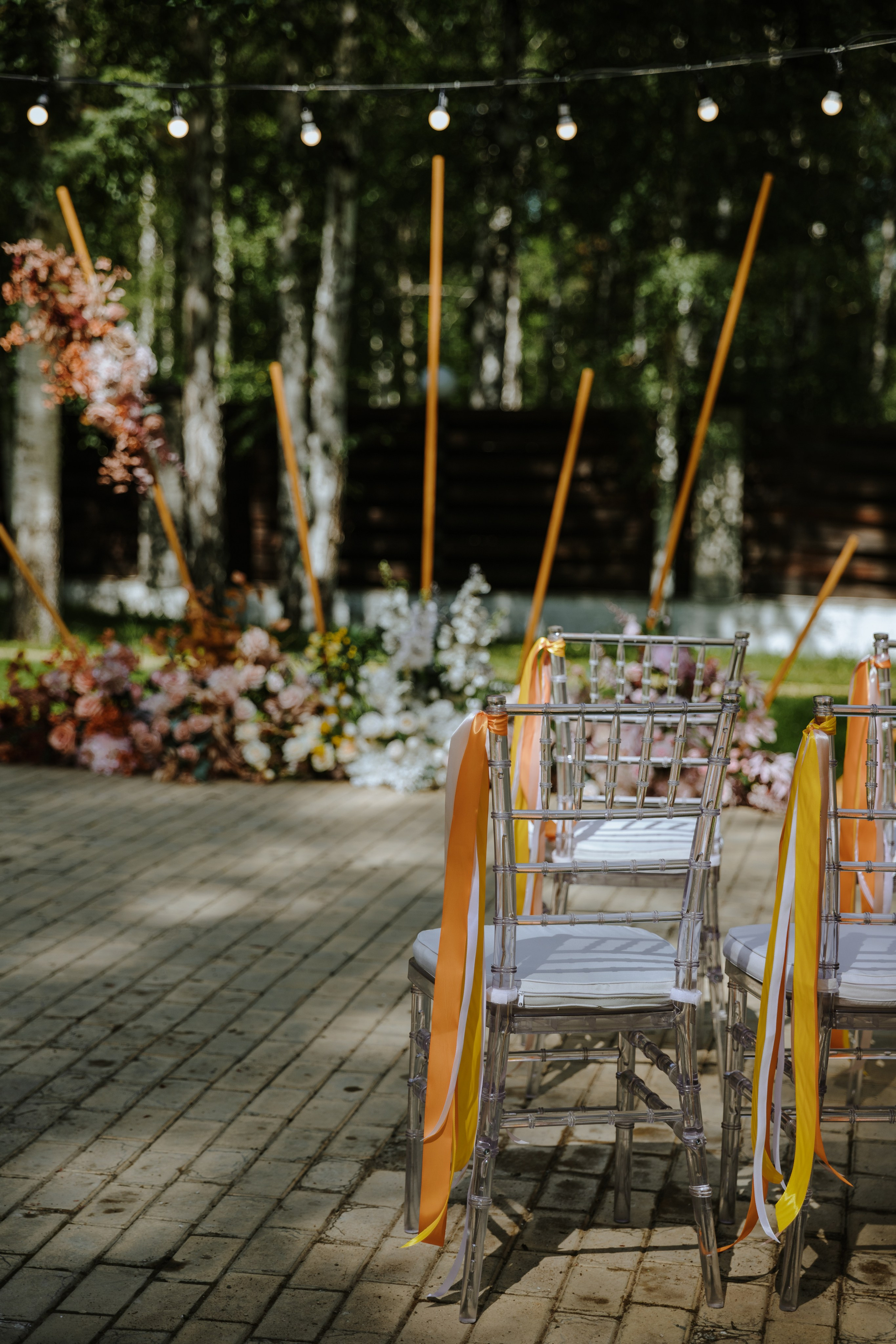 На переднем плане стулья украшенные для свадьбы, на заднем плане свадебная арка.