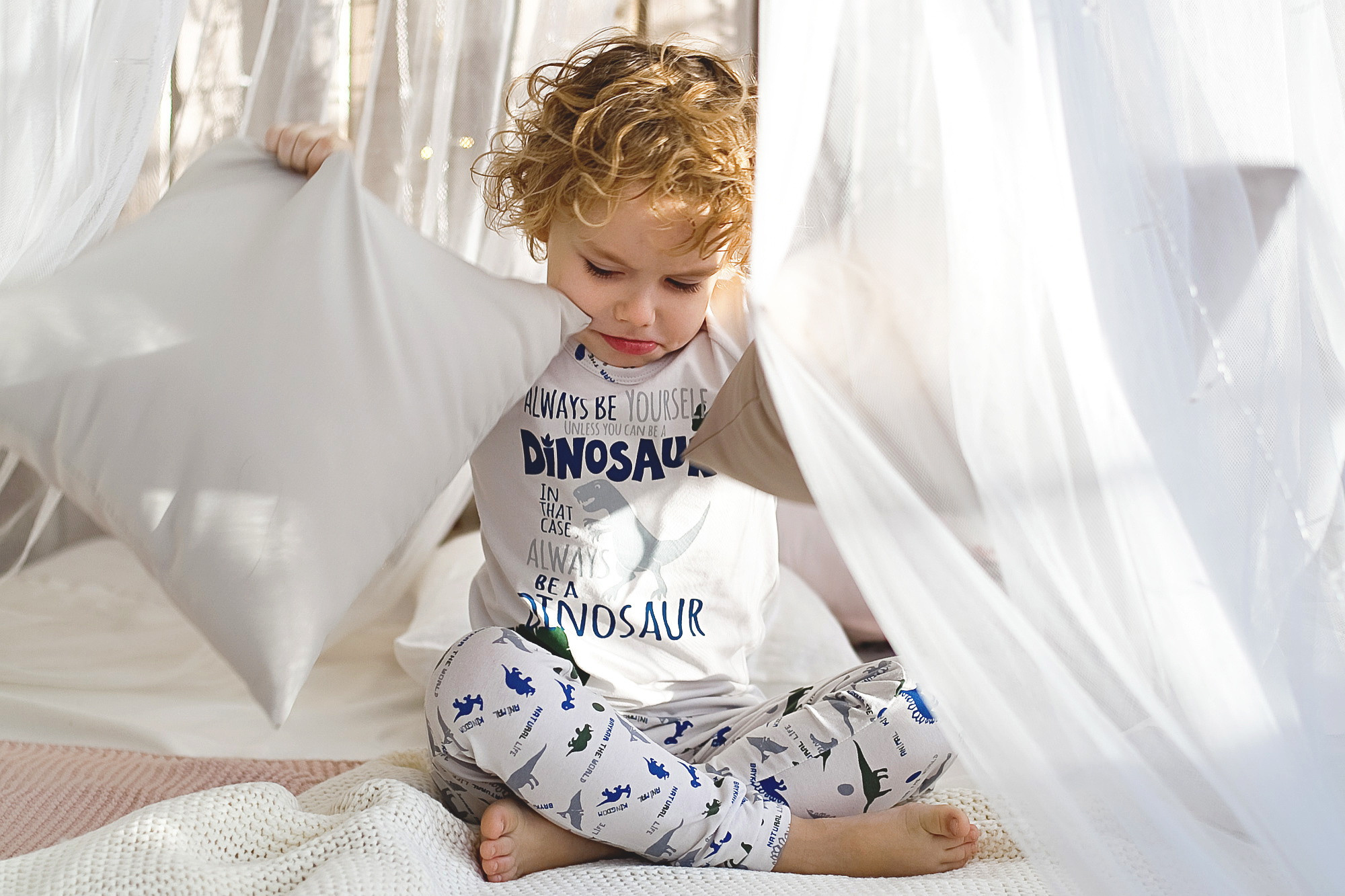 кудрявый мальчик на кровати с подушками