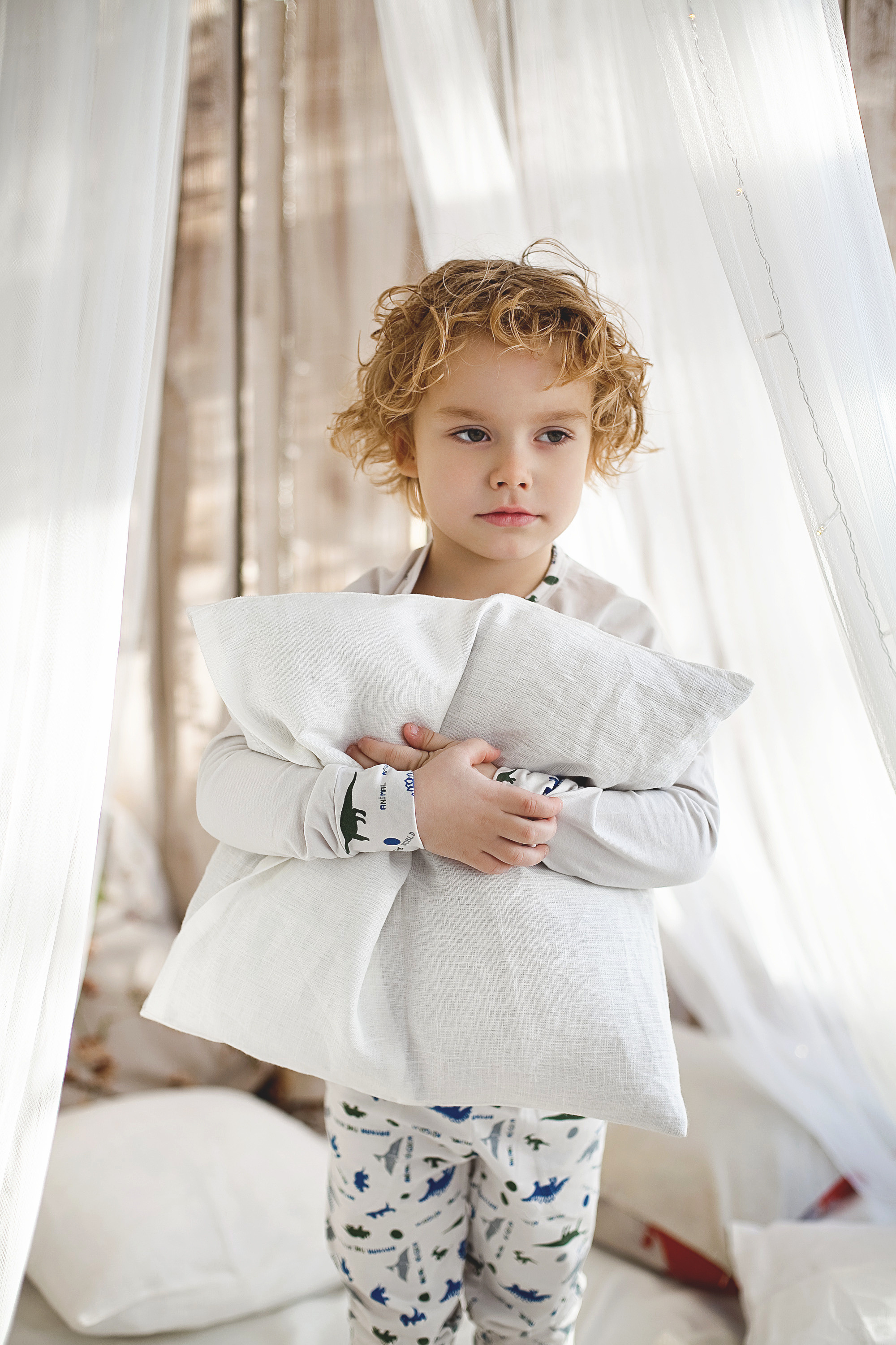 кудрявый мальчик обнимает подушку