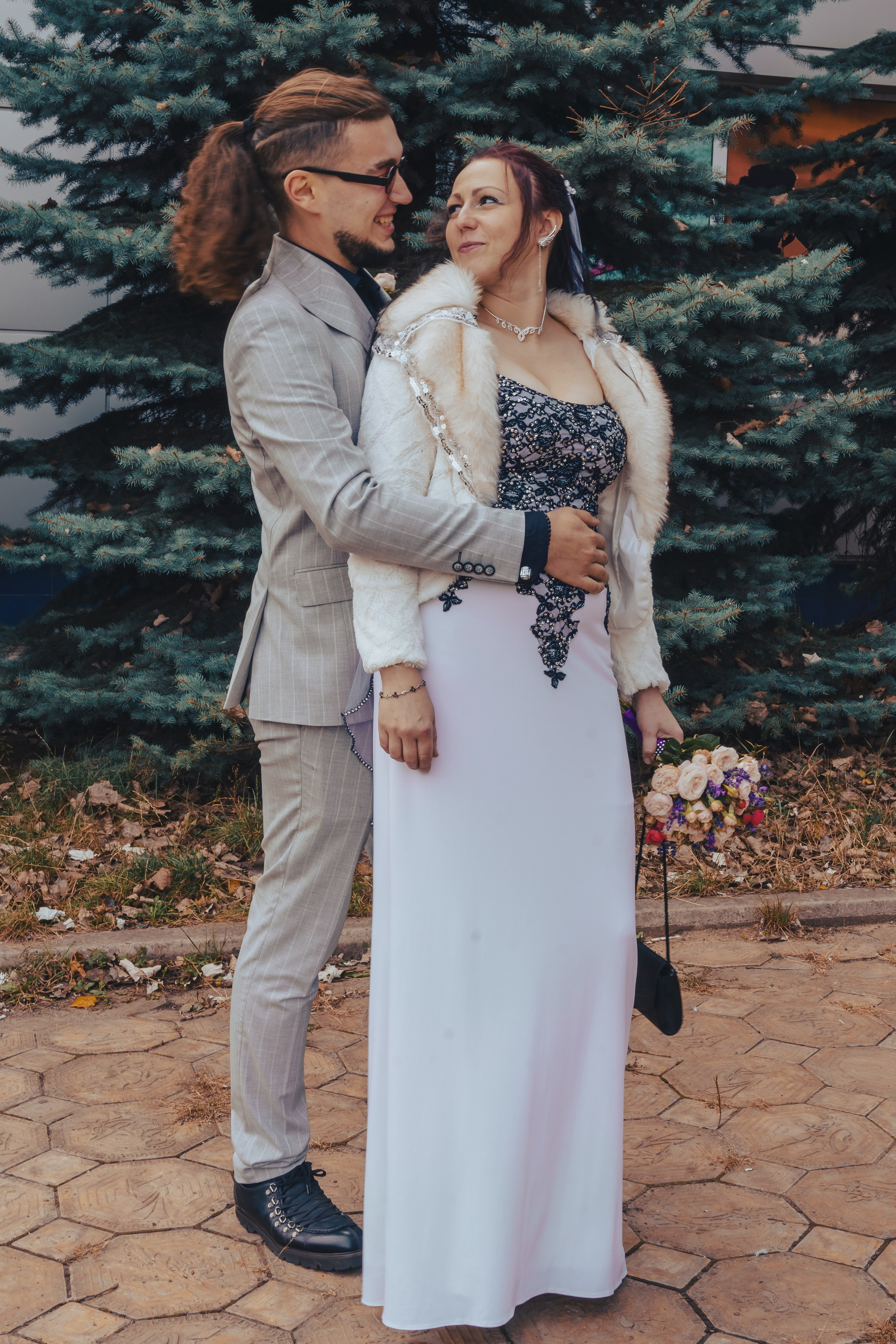 жених и невеста позируют на улице, жених обнимает невесту, невеста поворачивается к жениху