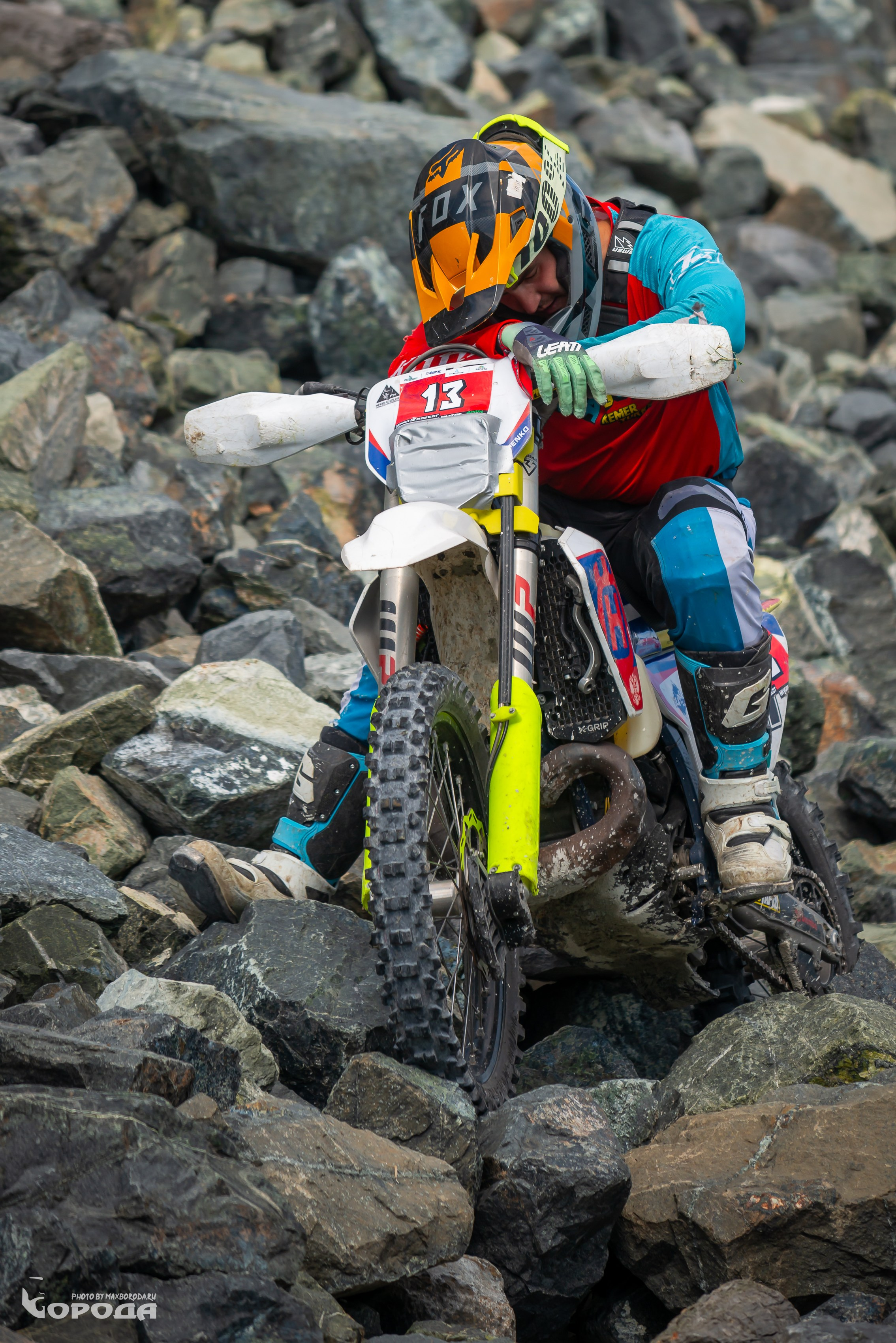 Мотокроссмен в шлеме FOX штурмует сложный каменистый участок, номер 13.