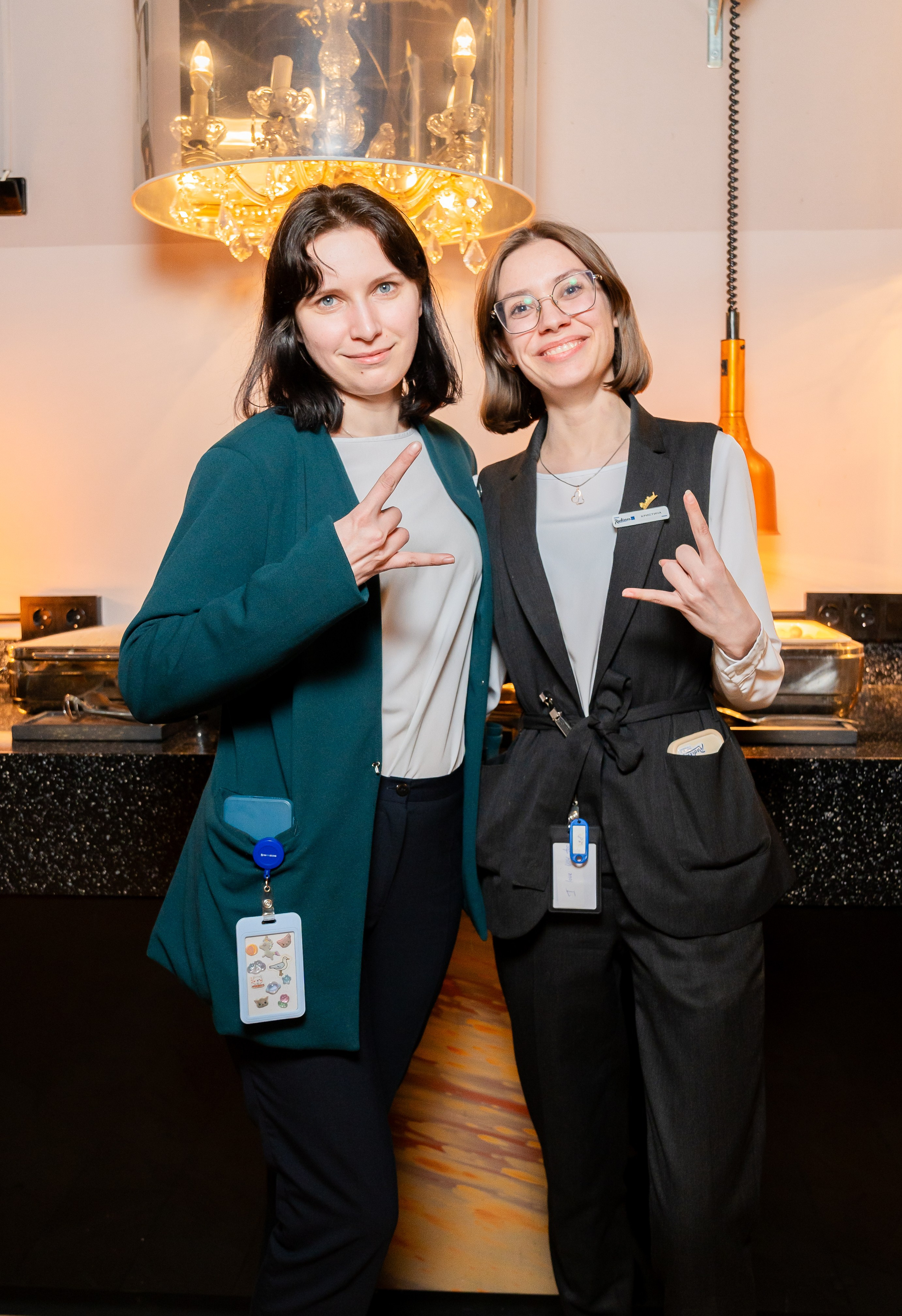 Две девушки-организатора в униформе позируют и показывают жест «рок» на мероприятии в Radisson Sonya. Фото Евгения Мальцева (evrednix.ru).